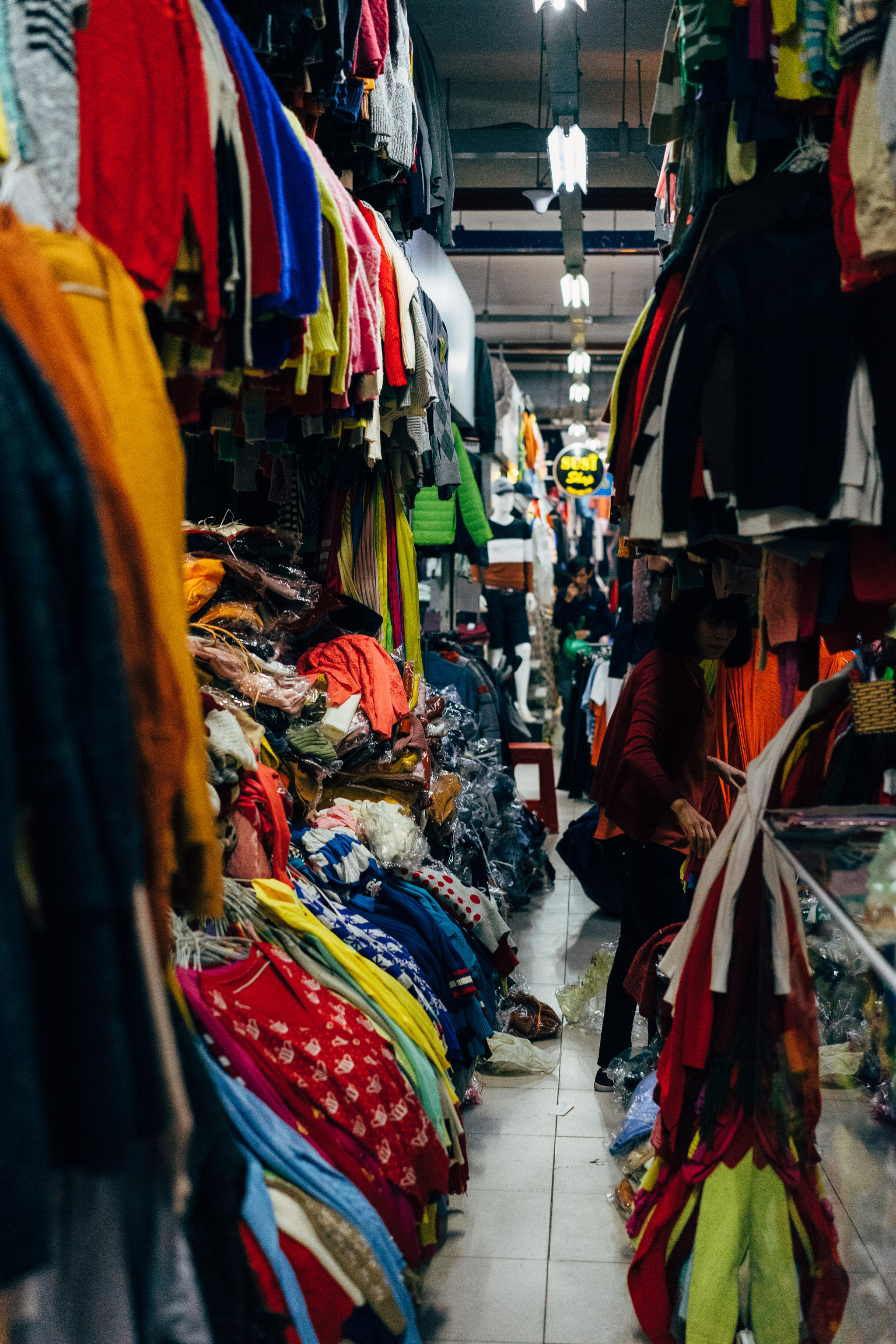 Da Lat market clothing stall with colorful clothes hanging and stacked.