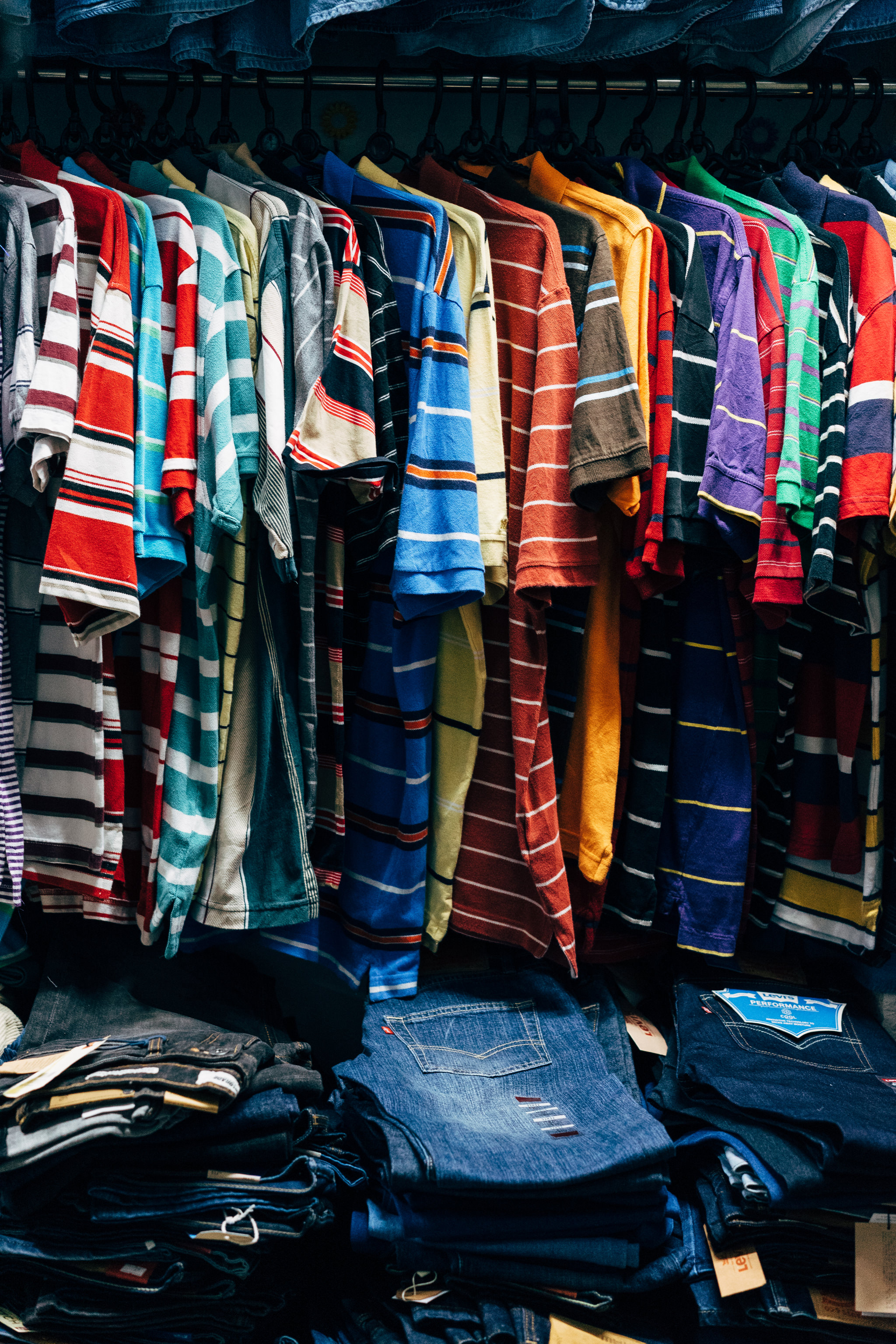 Colorful striped shirts hanging on a rack above stacks of jeans.