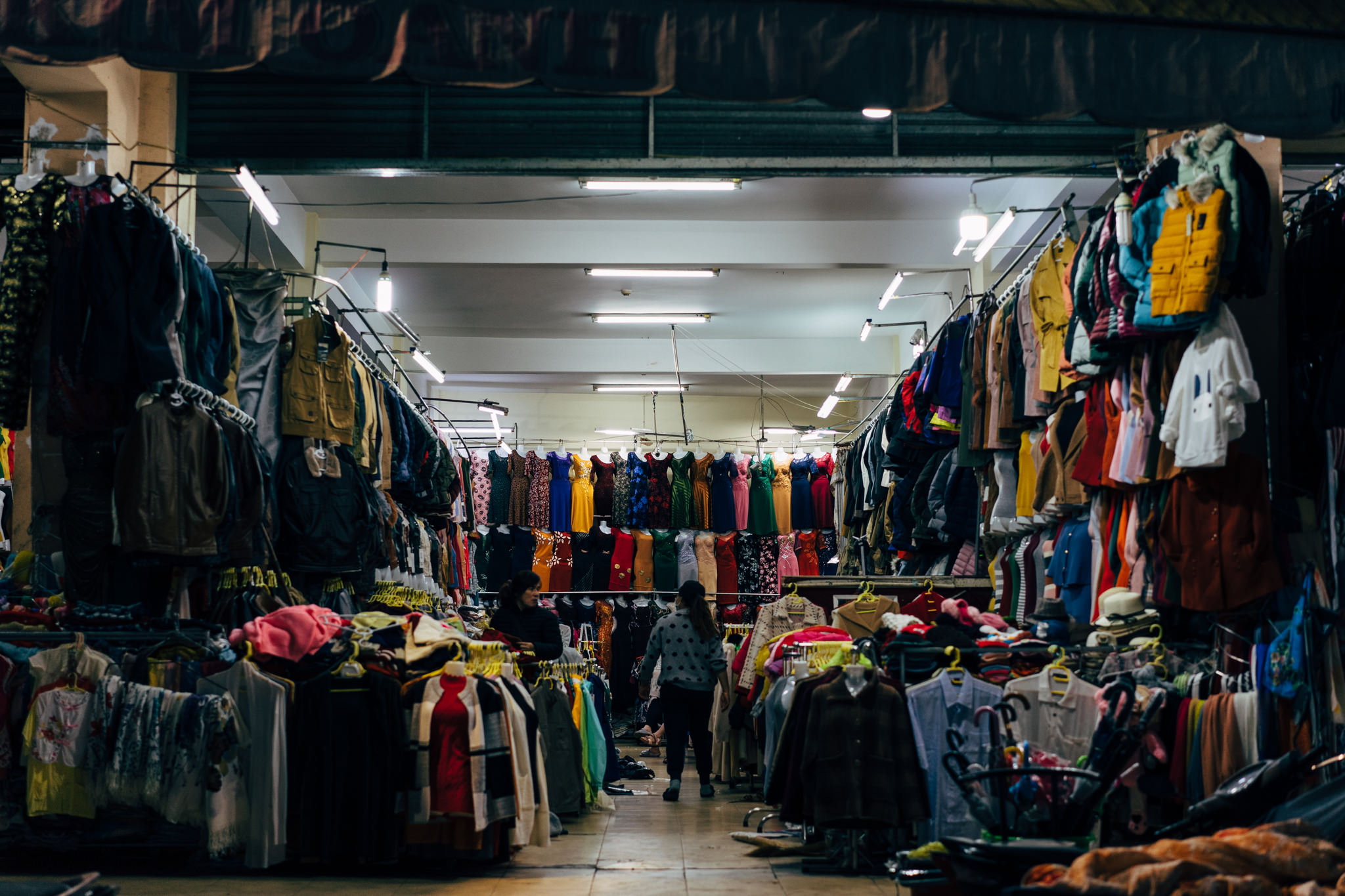 Interior of a clothing market in Da Lat, Vietnam, showing racks of clothing and two shoppers.