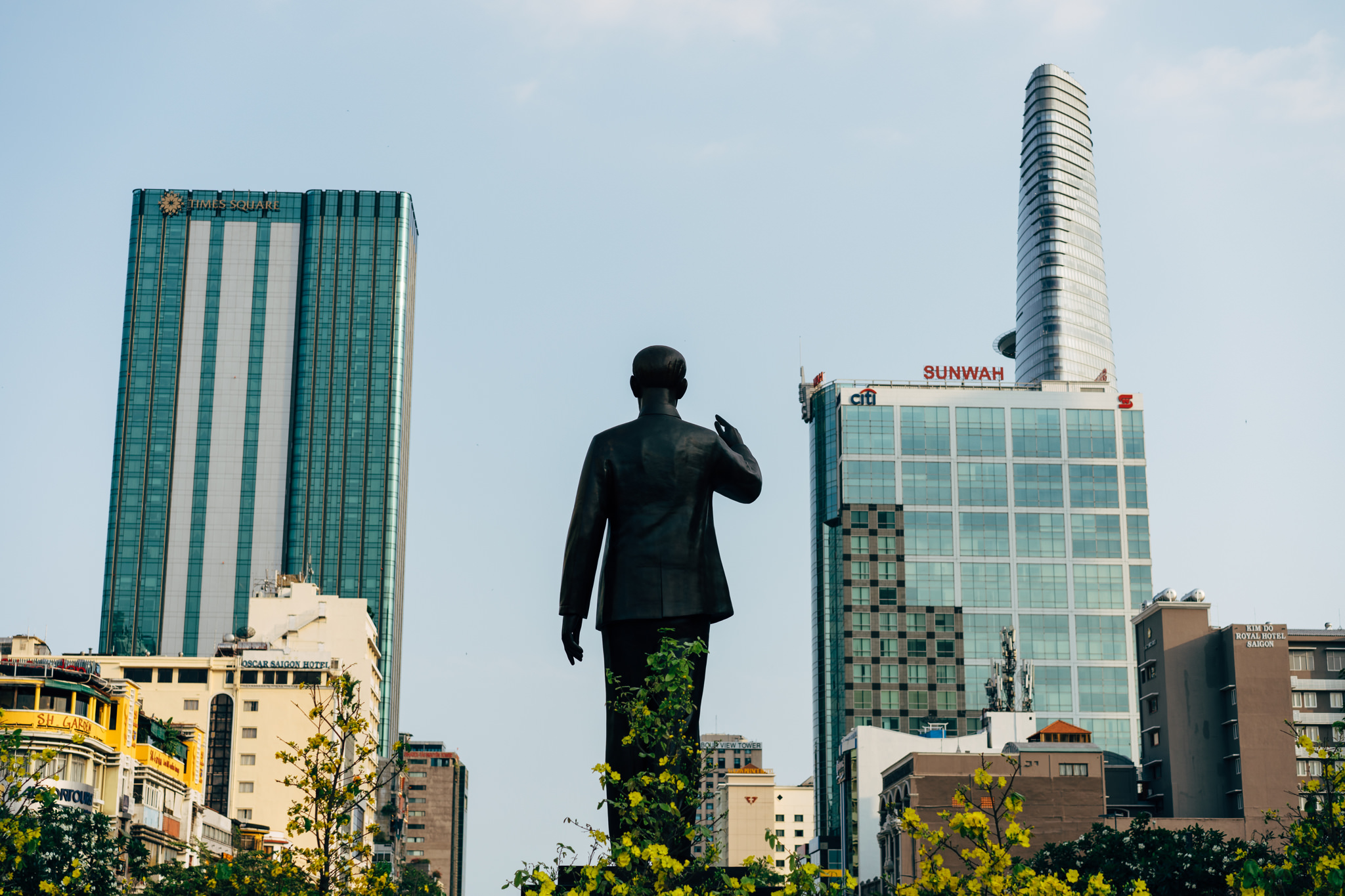 Bronze statue viewed from behind, with modern buildings in the background.