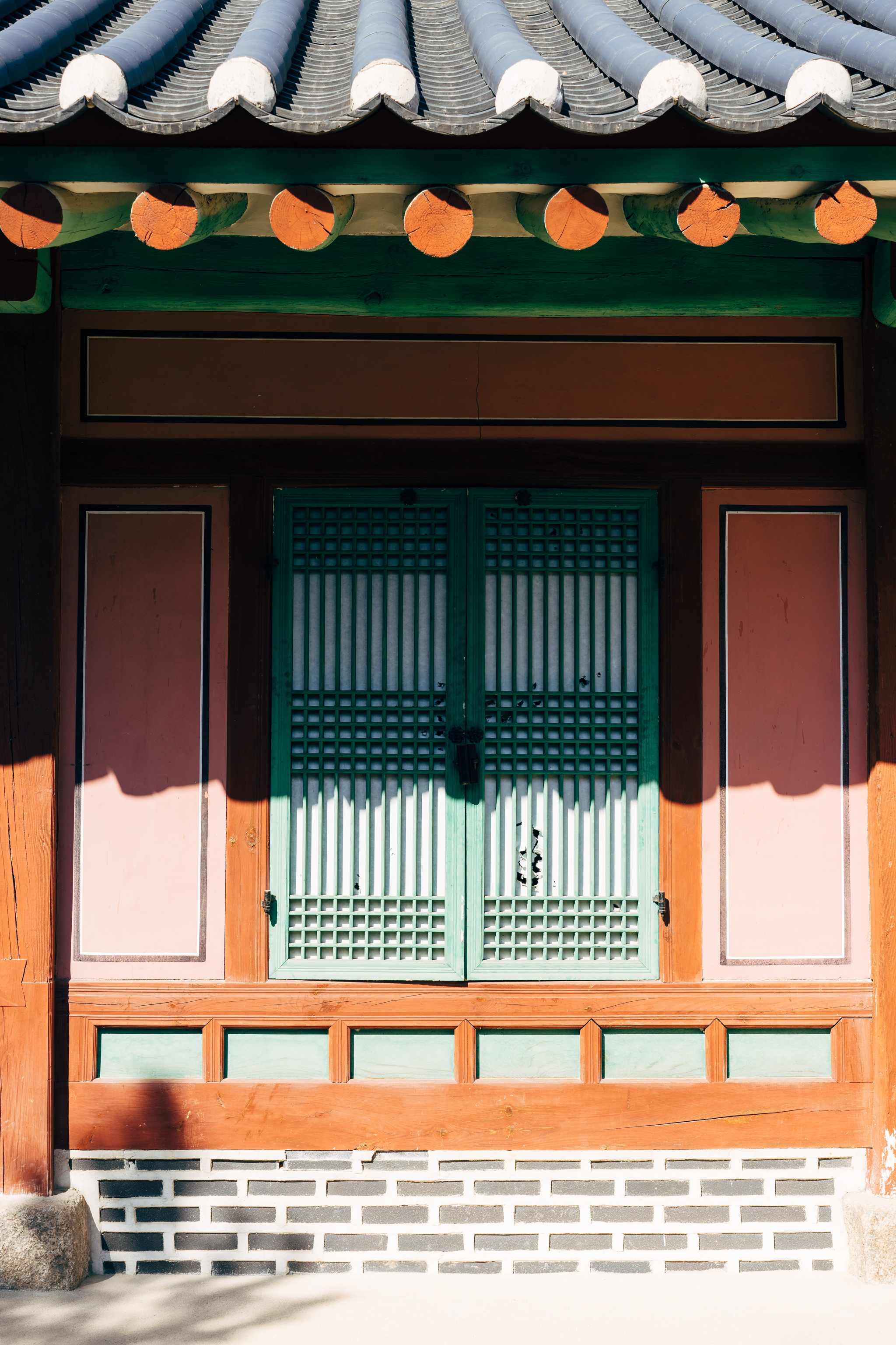 Green-framed doors with a traditional Korean lattice design set within a wooden structure with a tiled roof.