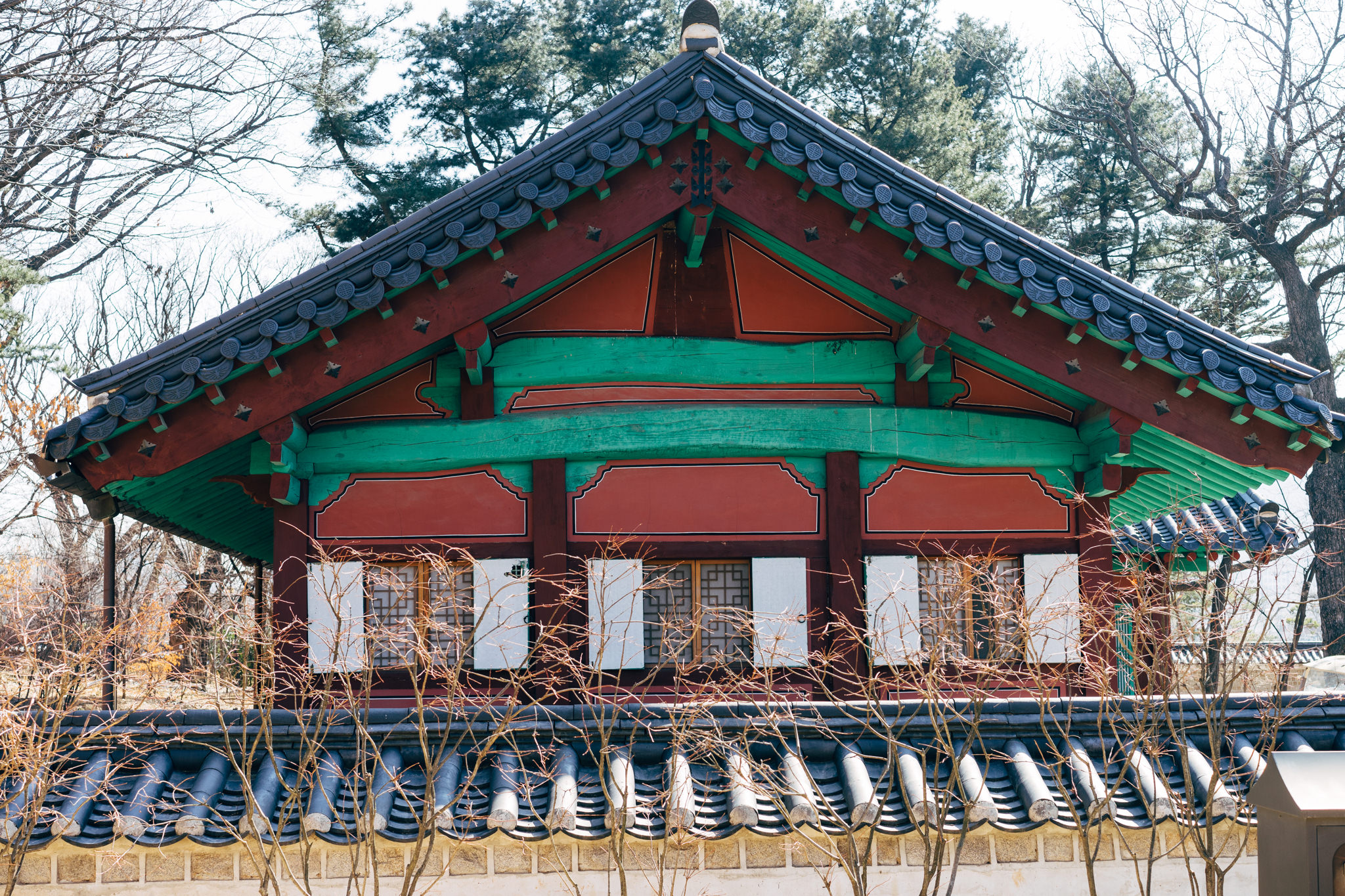 Jongmyo Shrine building with teal and red painted wood, dark gray roof tiles, and white-framed windows.