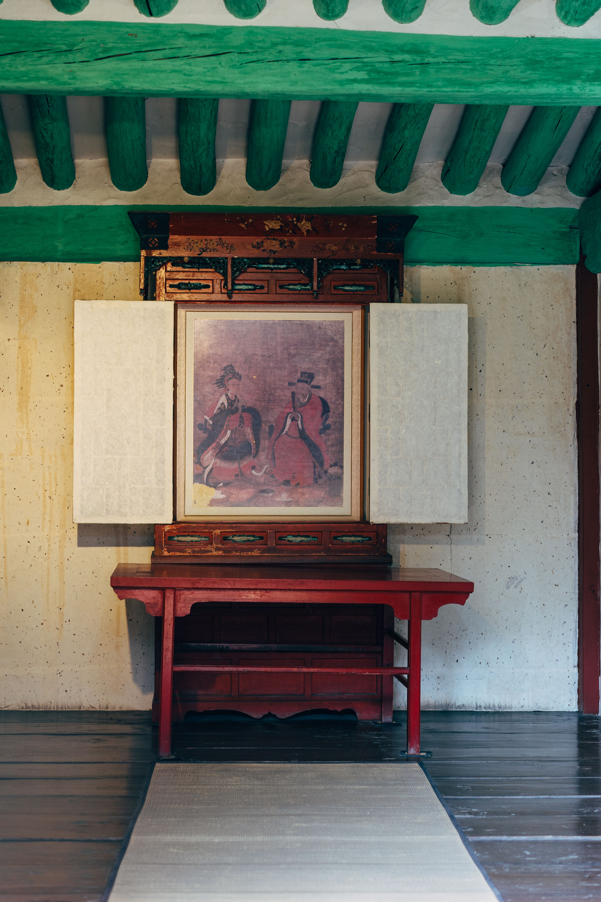 Interior view of Jongmyo Shrine in Seoul, showing a red table and an ornate wooden cabinet with a painting of two figures in traditional clothing.