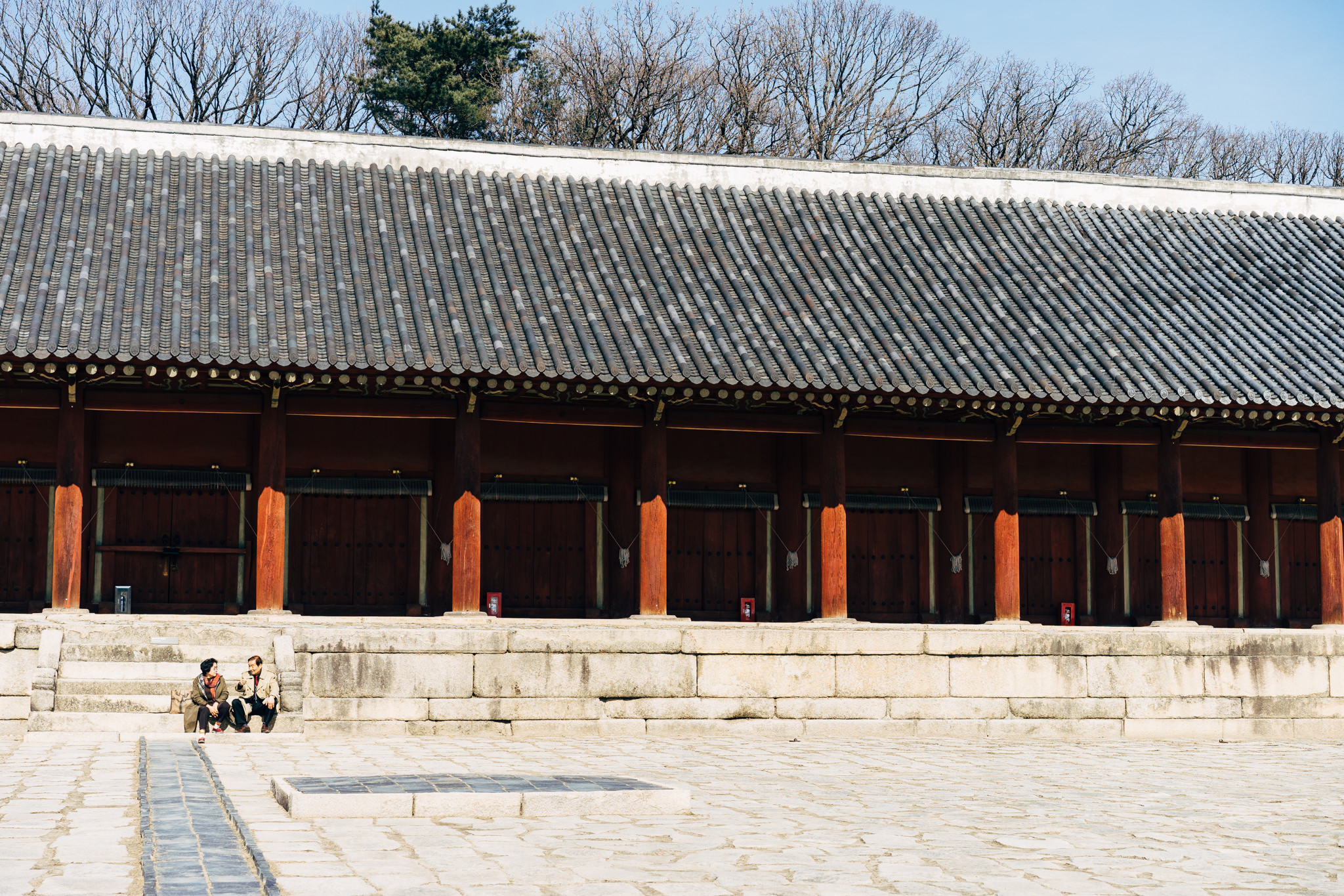 Two people sitting in front of Jongmyo Shrine in Seoul.