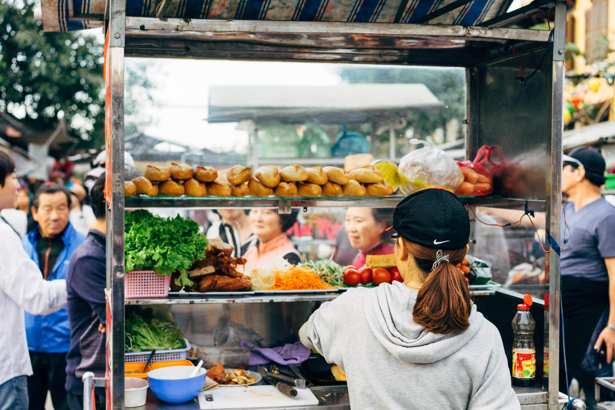 Woman preparing banh mi at a street food stand.