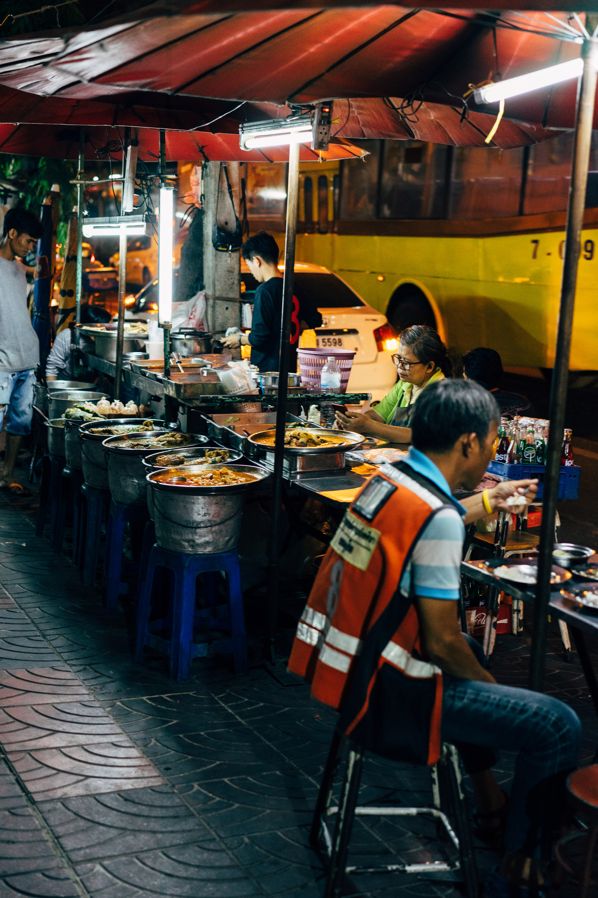 Bangkok night market food stalls with various dishes in metal containers.