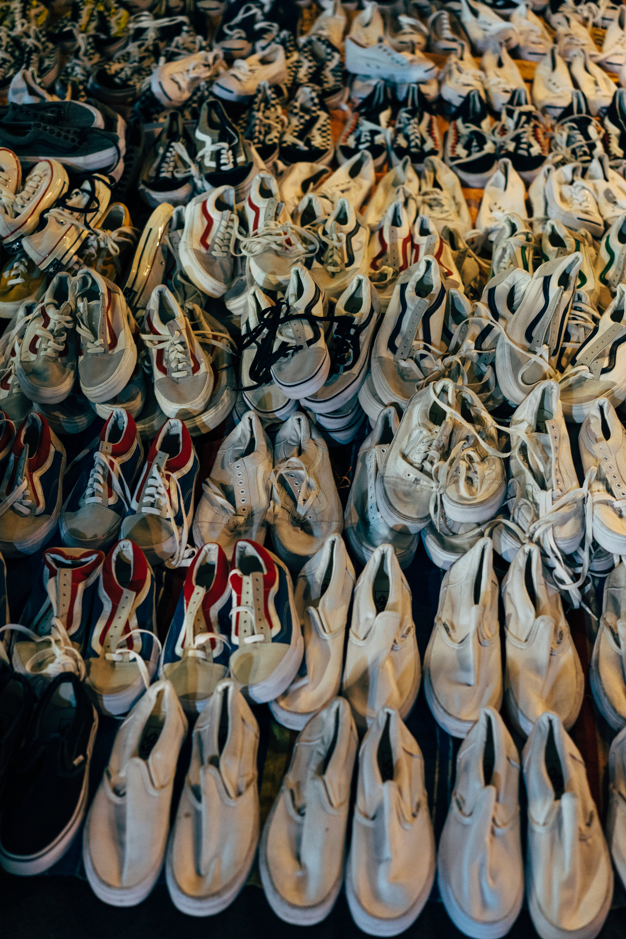 A large pile of used sneakers in various colors and styles at a Bangkok market.