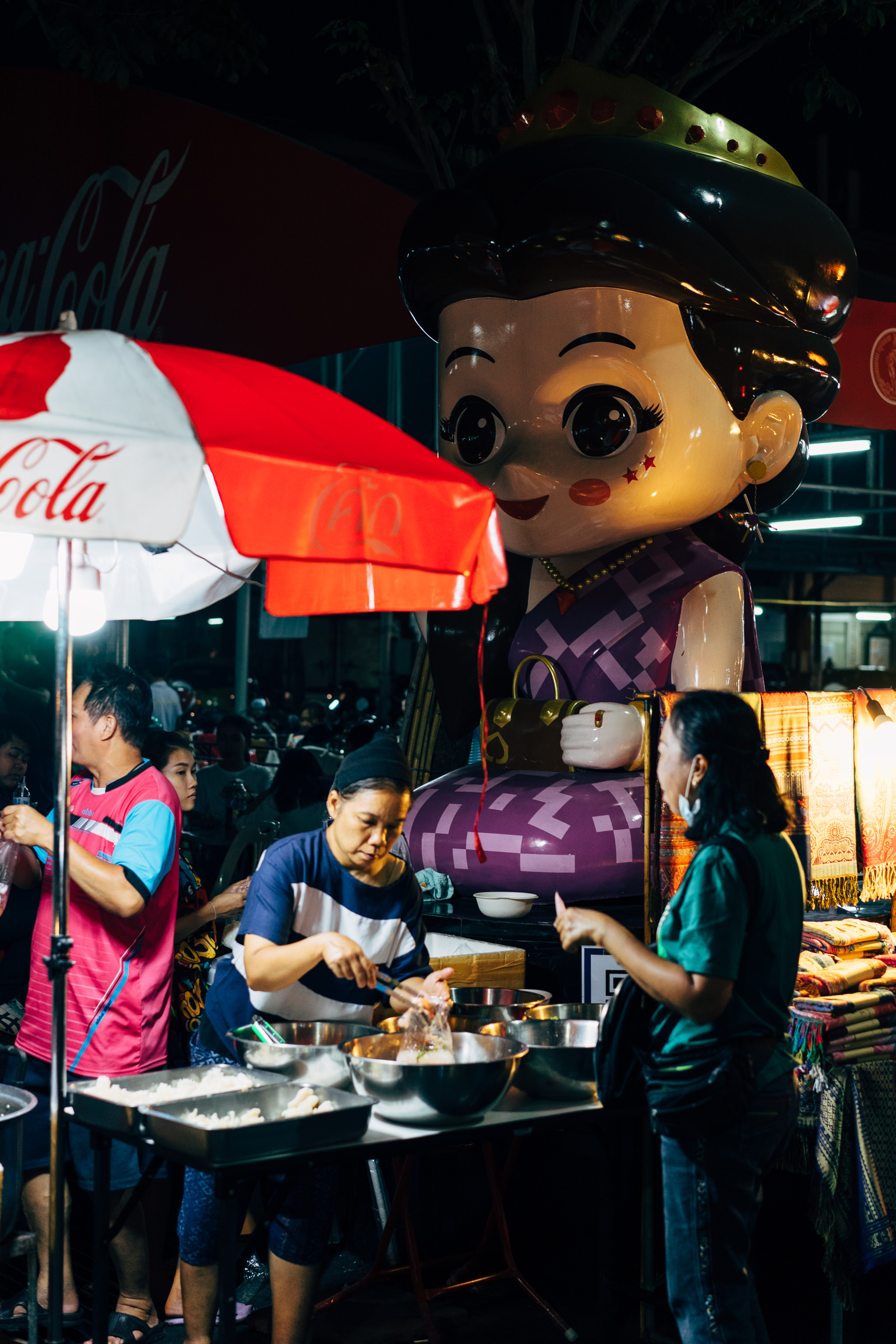 Night market scene in Bangkok with a large cartoon character and food vendors.