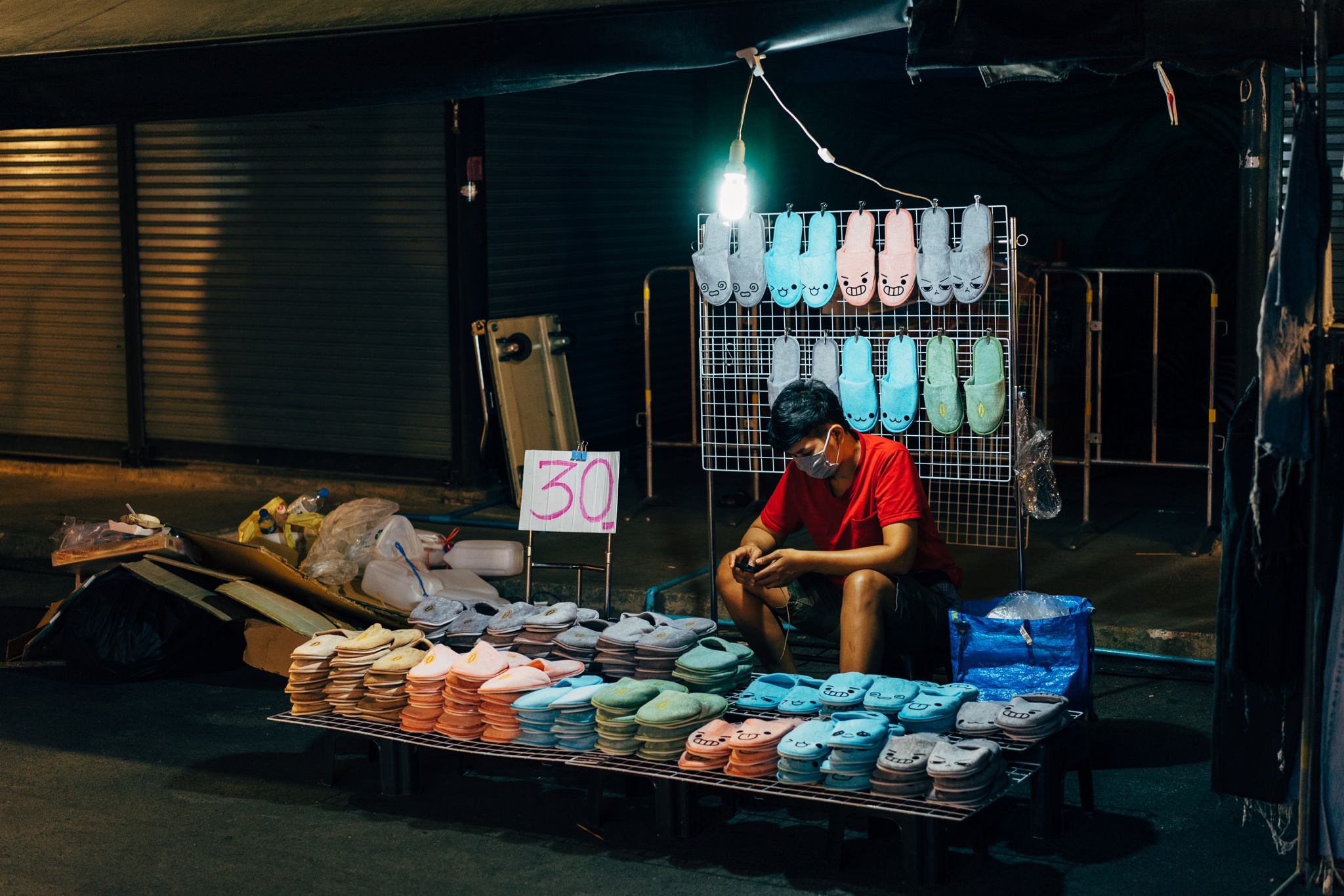 Bangkok night market stall selling flip-flops with cartoon faces.