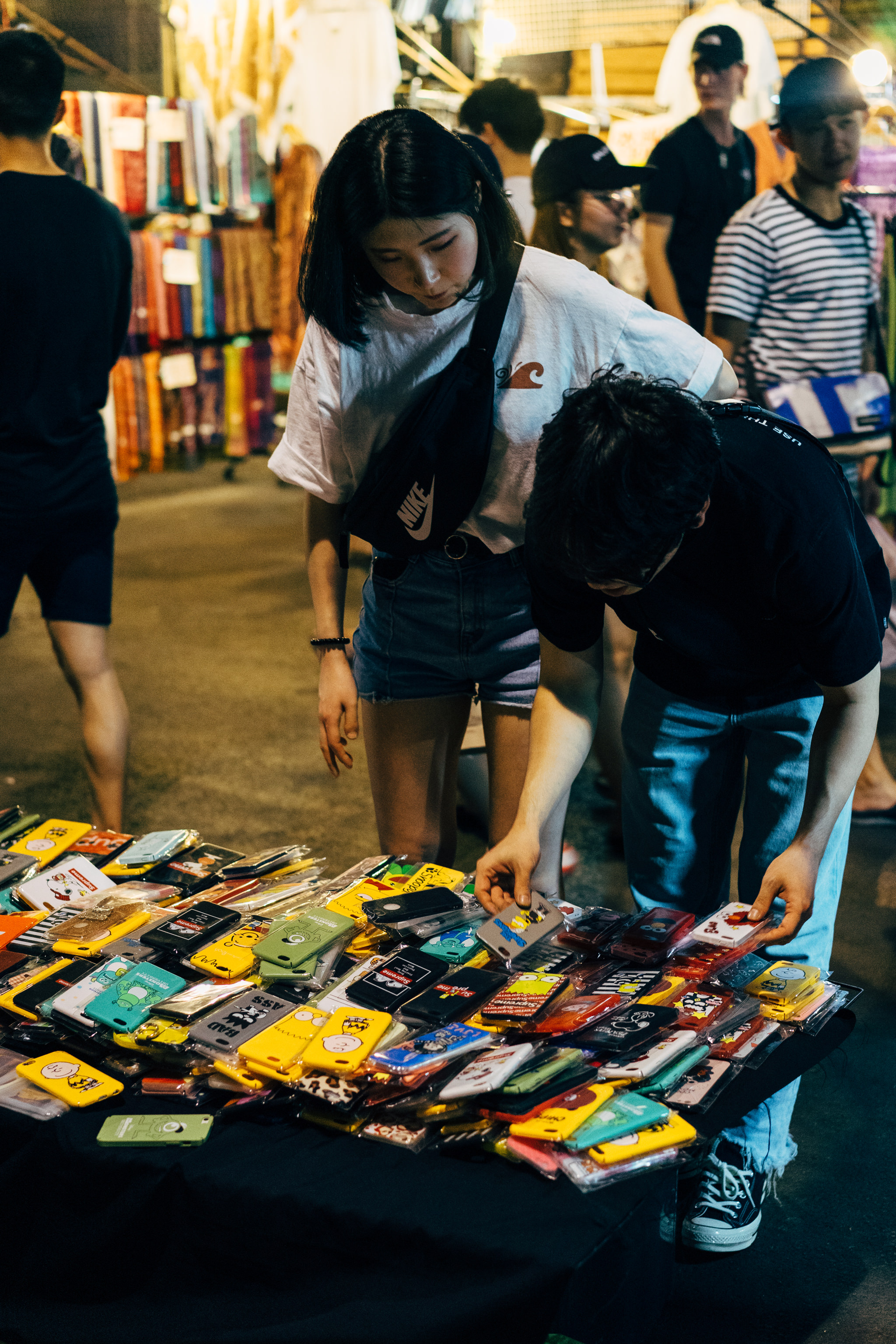Two people browsing colorful smartphone cases at a Bangkok market.