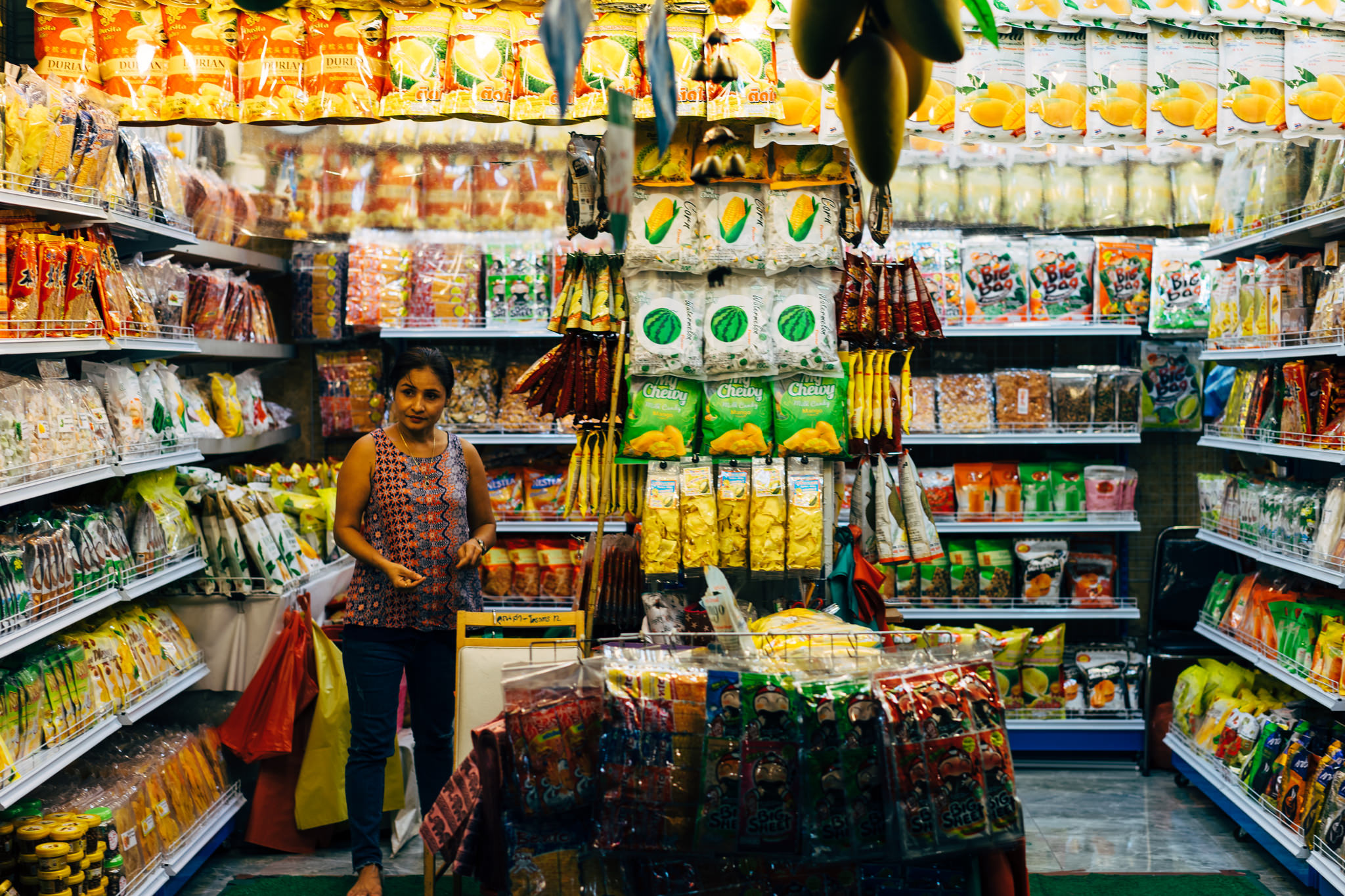 Woman standing in a Bangkok market surrounded by shelves of dried fruit and snacks.