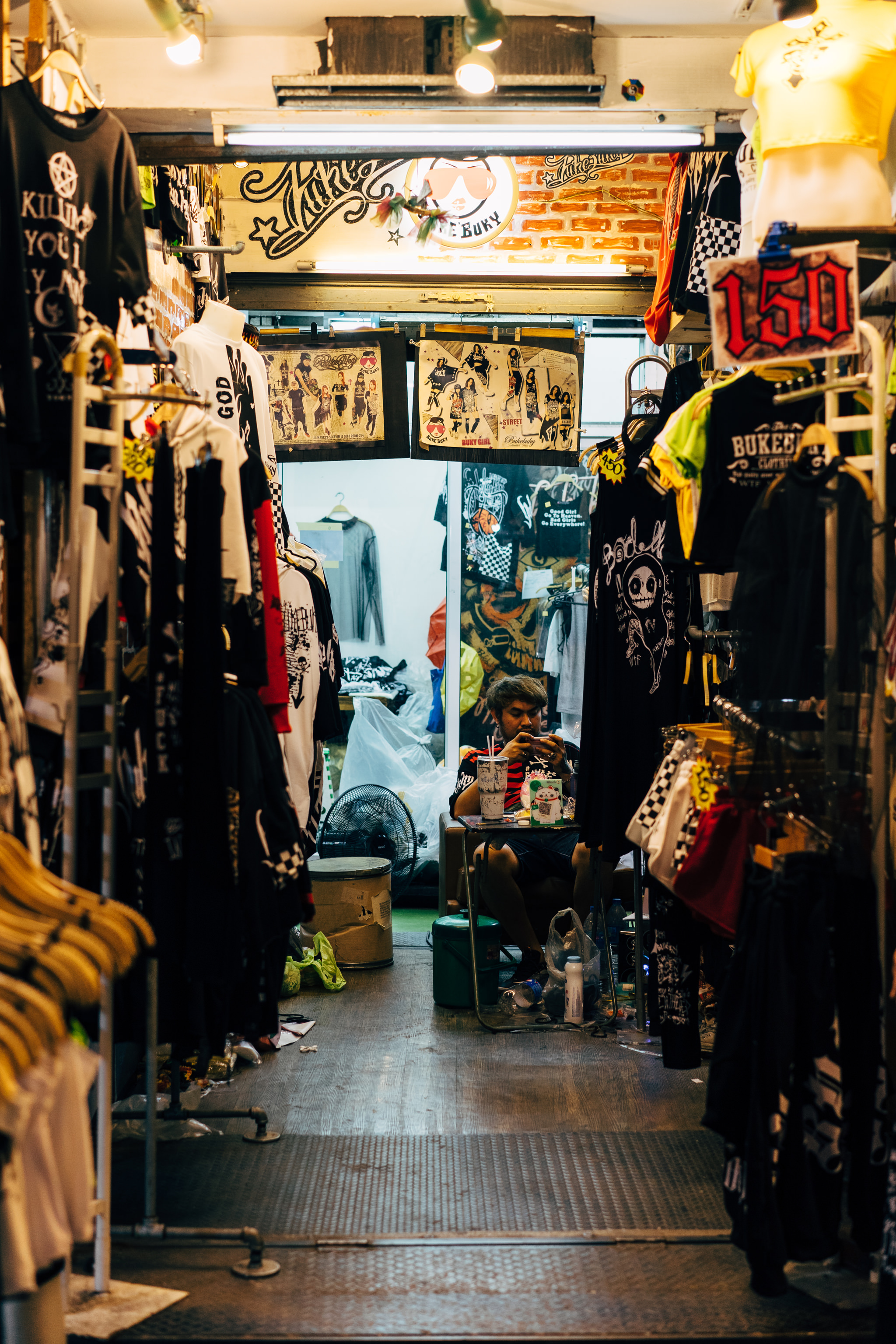 Bangkok market clothing stall with person on phone.