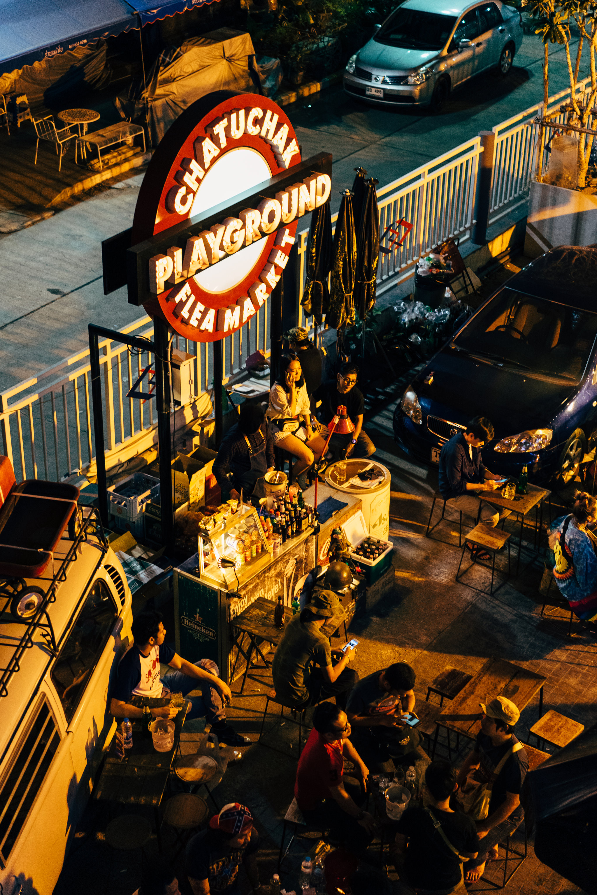 Chatuchak Playground Flea Market sign at night, people sitting at tables.