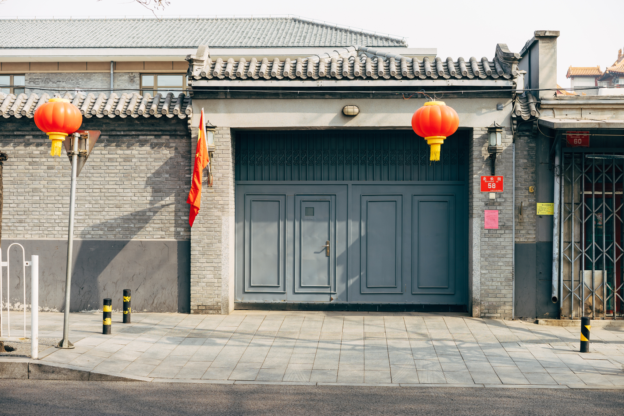 Gray building in Beijing with large gray door, red lanterns, and a Chinese flag.