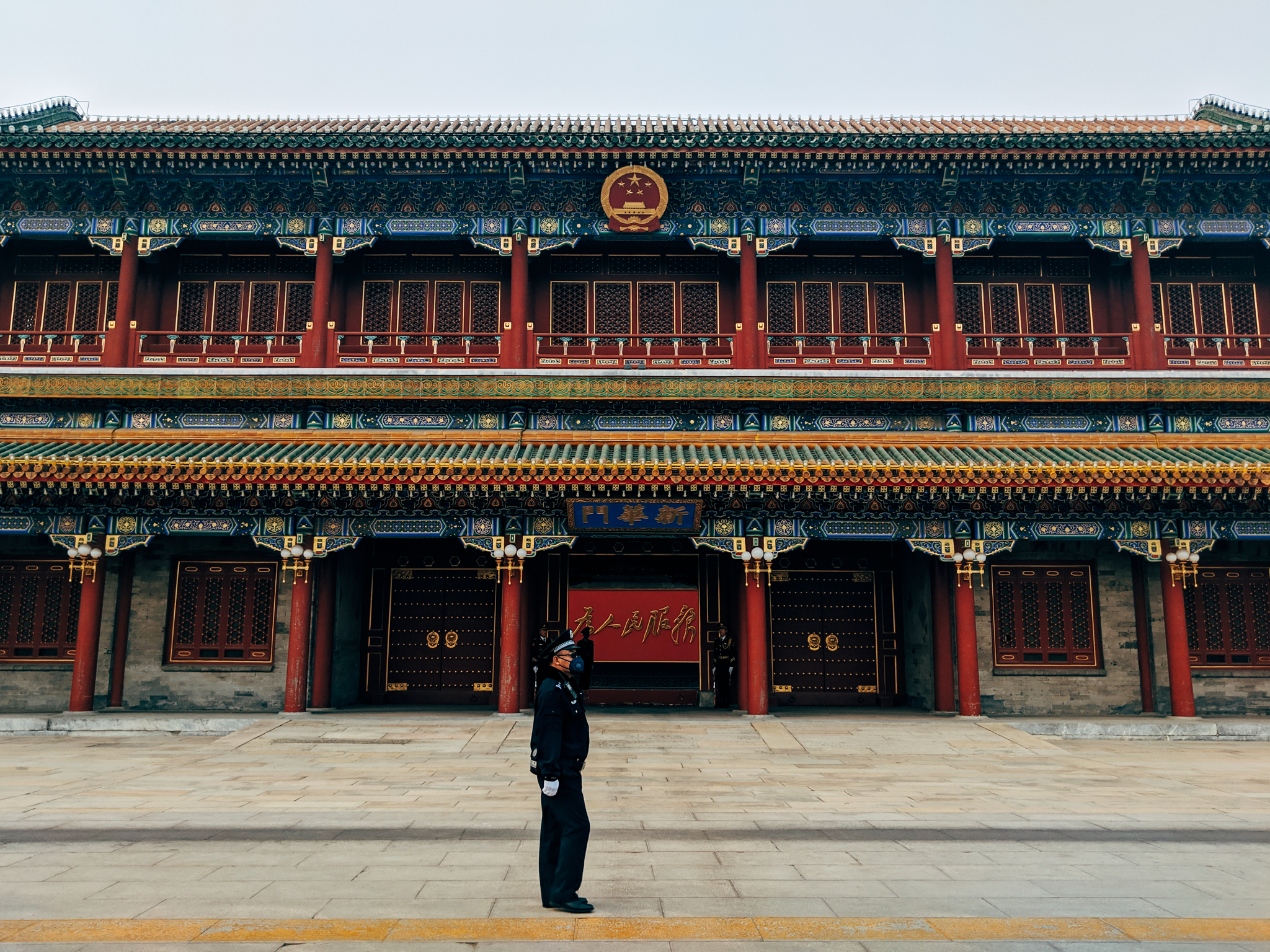 Guard standing in front of ornate red and blue building in Beijing.
