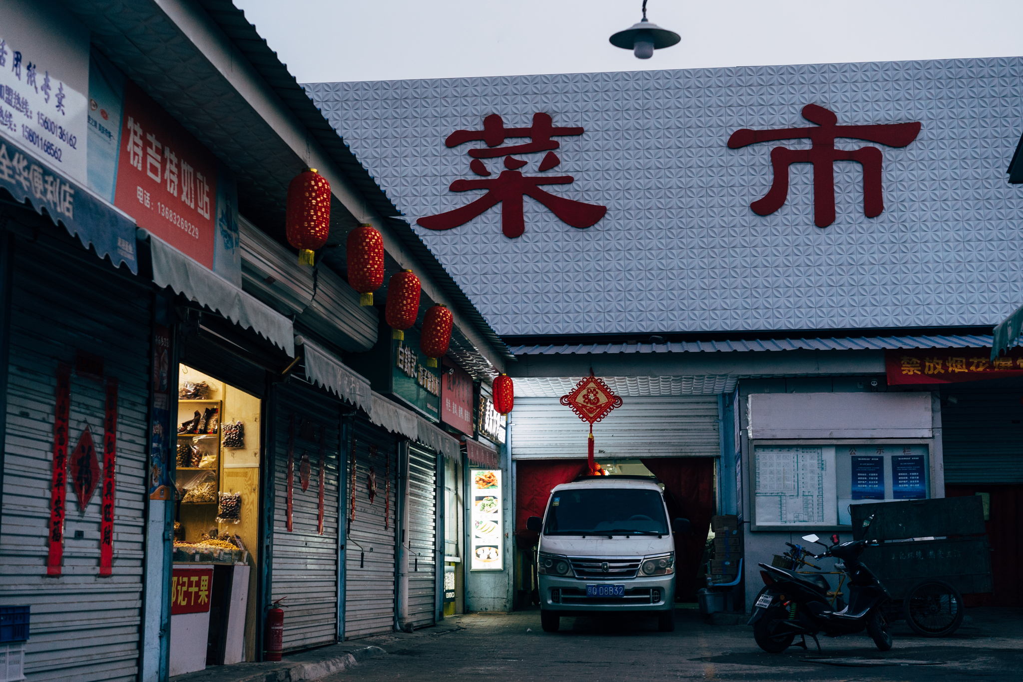 Beijing alleyway at dusk with shops and a van; large red Chinese characters on a building.
