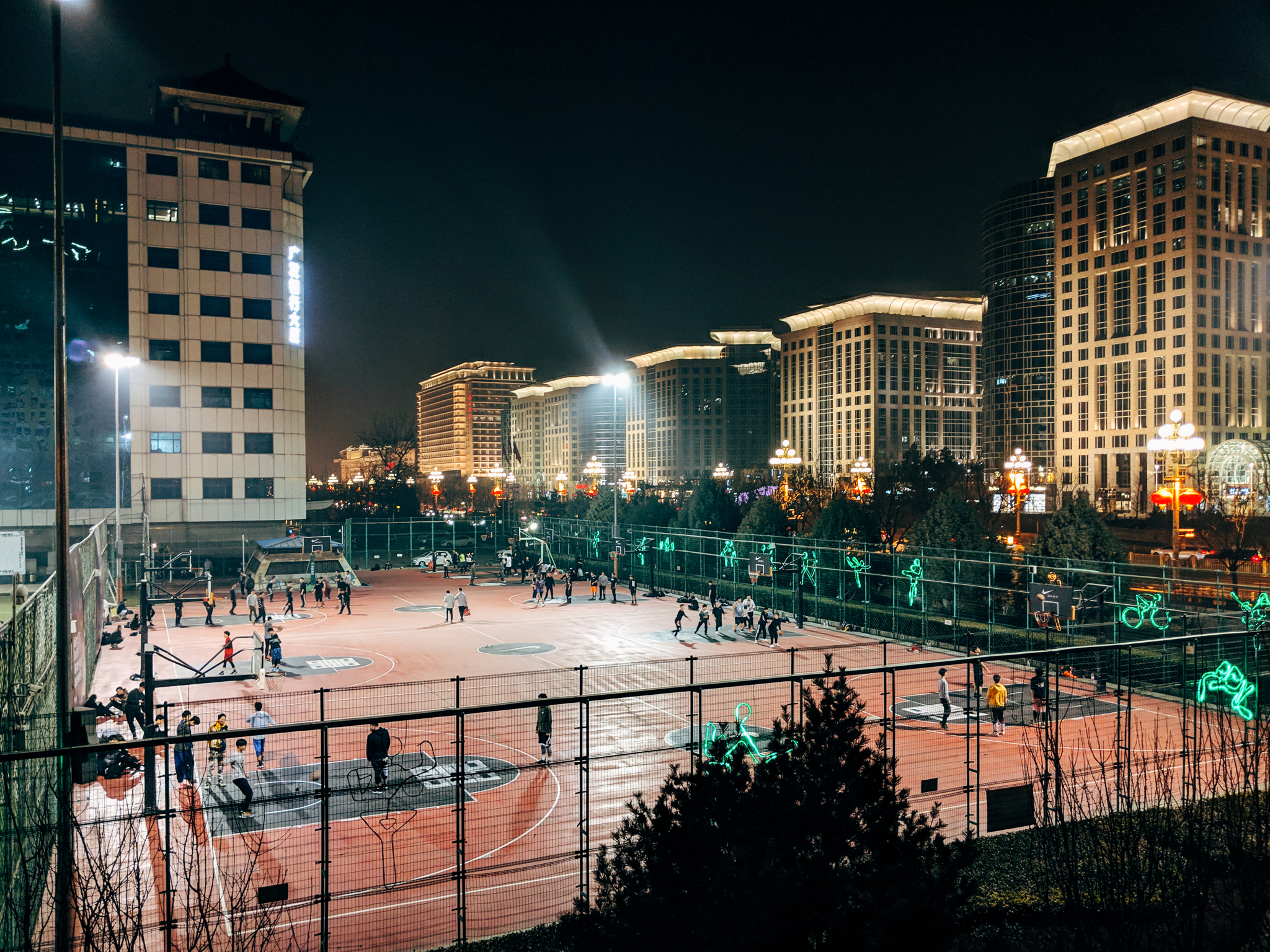 Night view of a basketball court in Beijing, China, with people playing and buildings in the background.