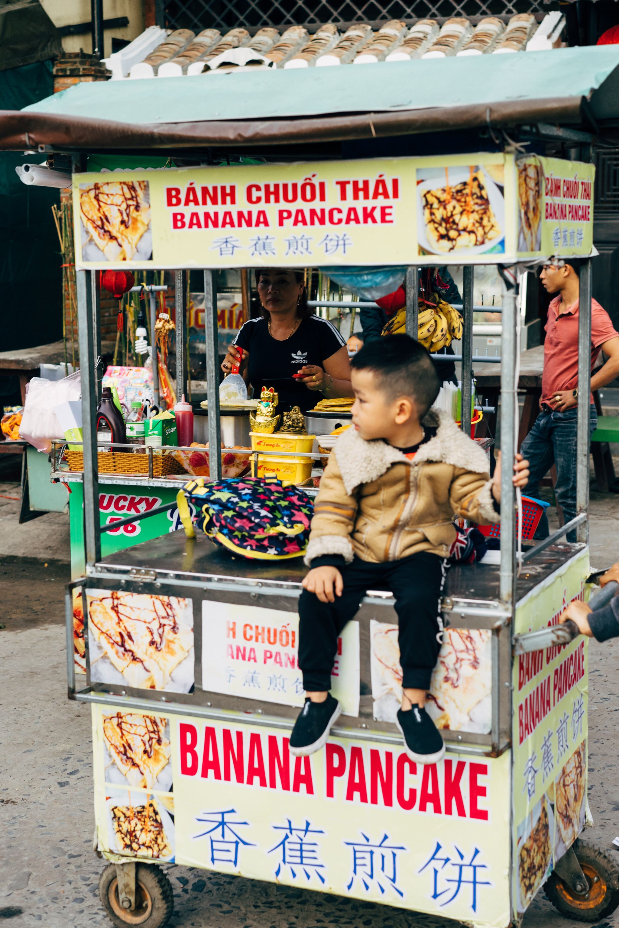 Young boy sitting on a banana pancake food cart.