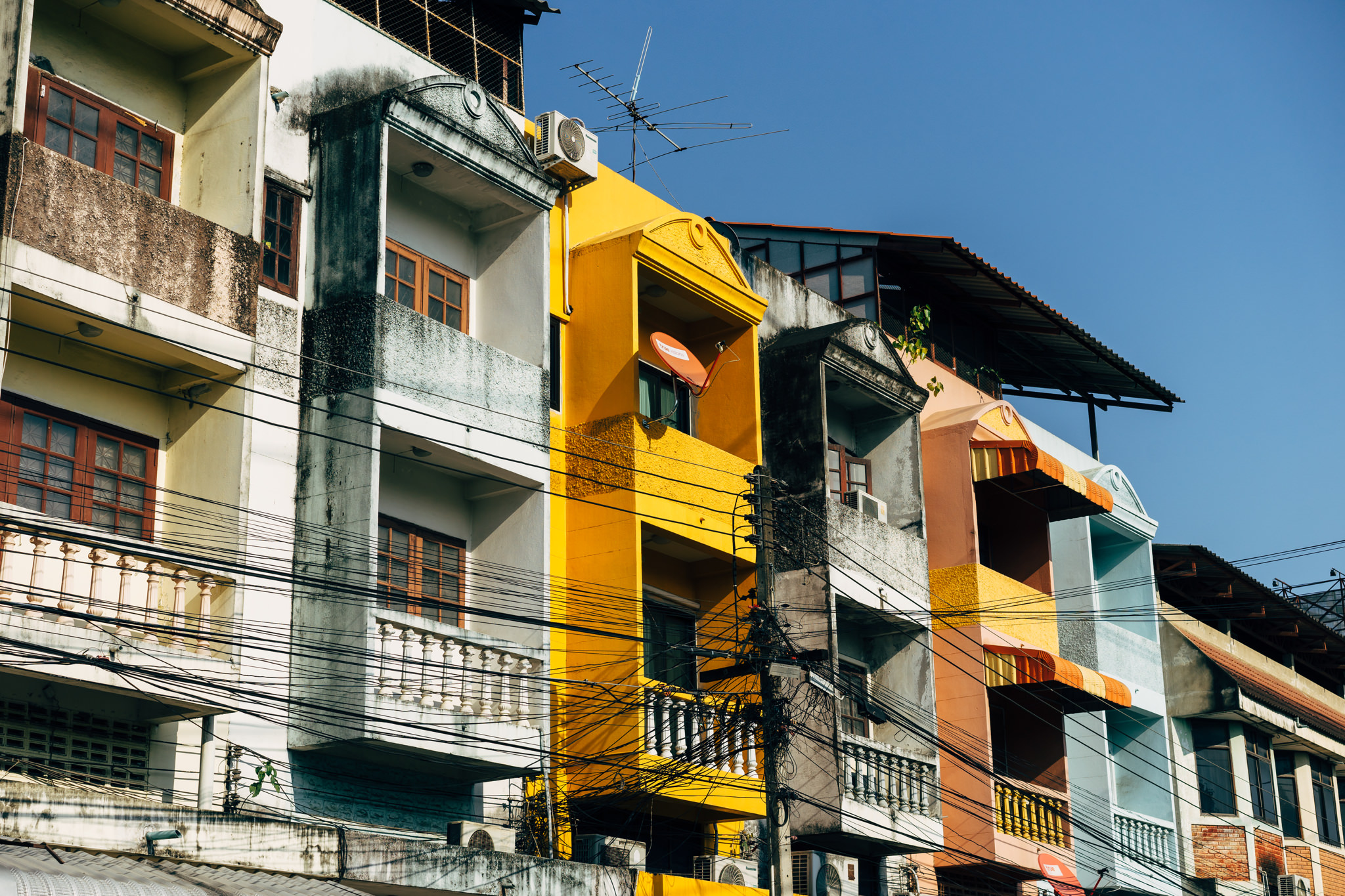 Close-up of colorful multi-story buildings in Chiang Mai, Thailand, with numerous electrical wires.