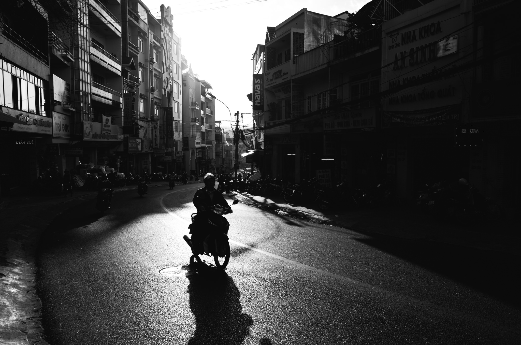 Silhouette of person on motorbike on sunlit Dalat street.