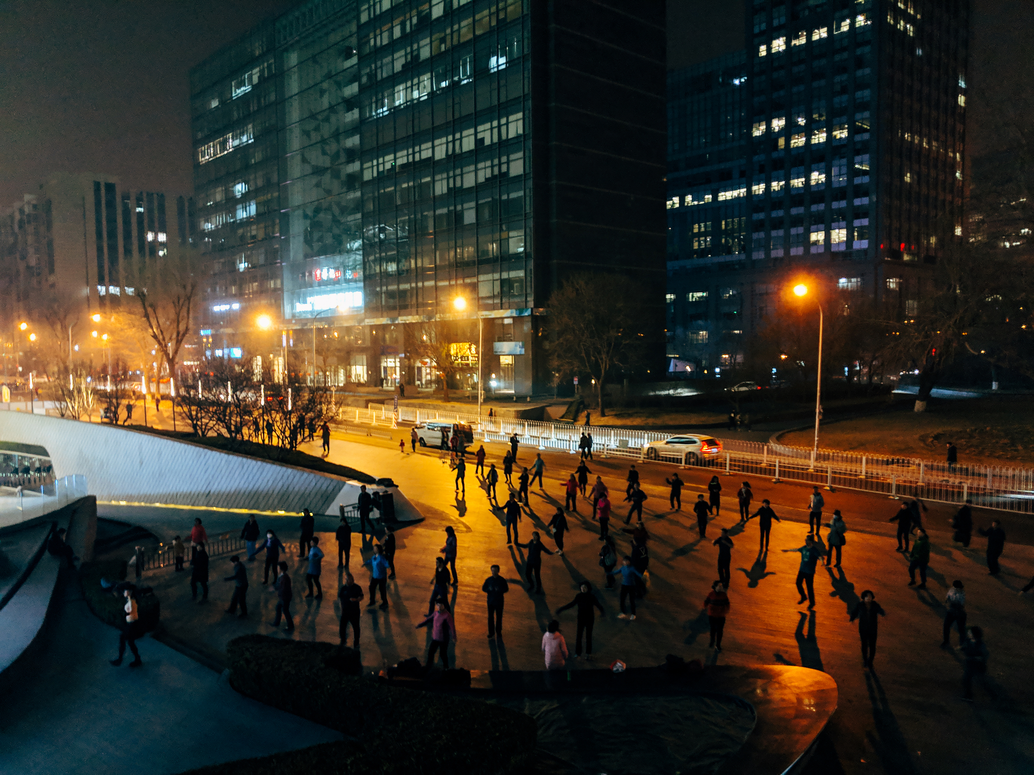 Nighttime aerial view of people dancing in a city square in Beijing, China.