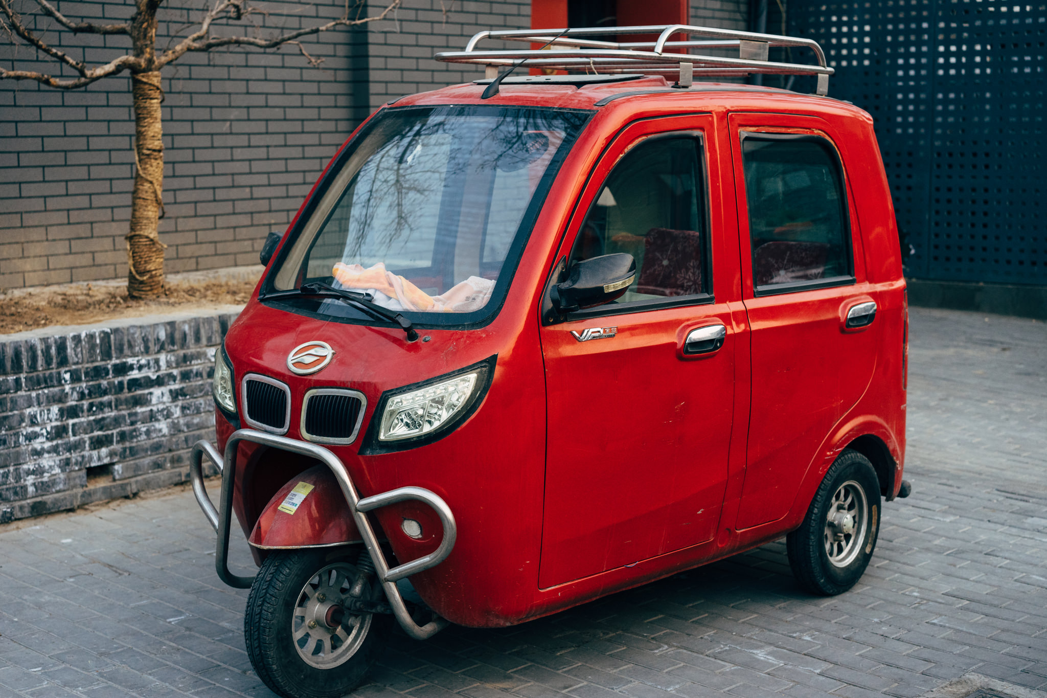 Red electric vehicle with a roof rack parked on a cobblestone street.