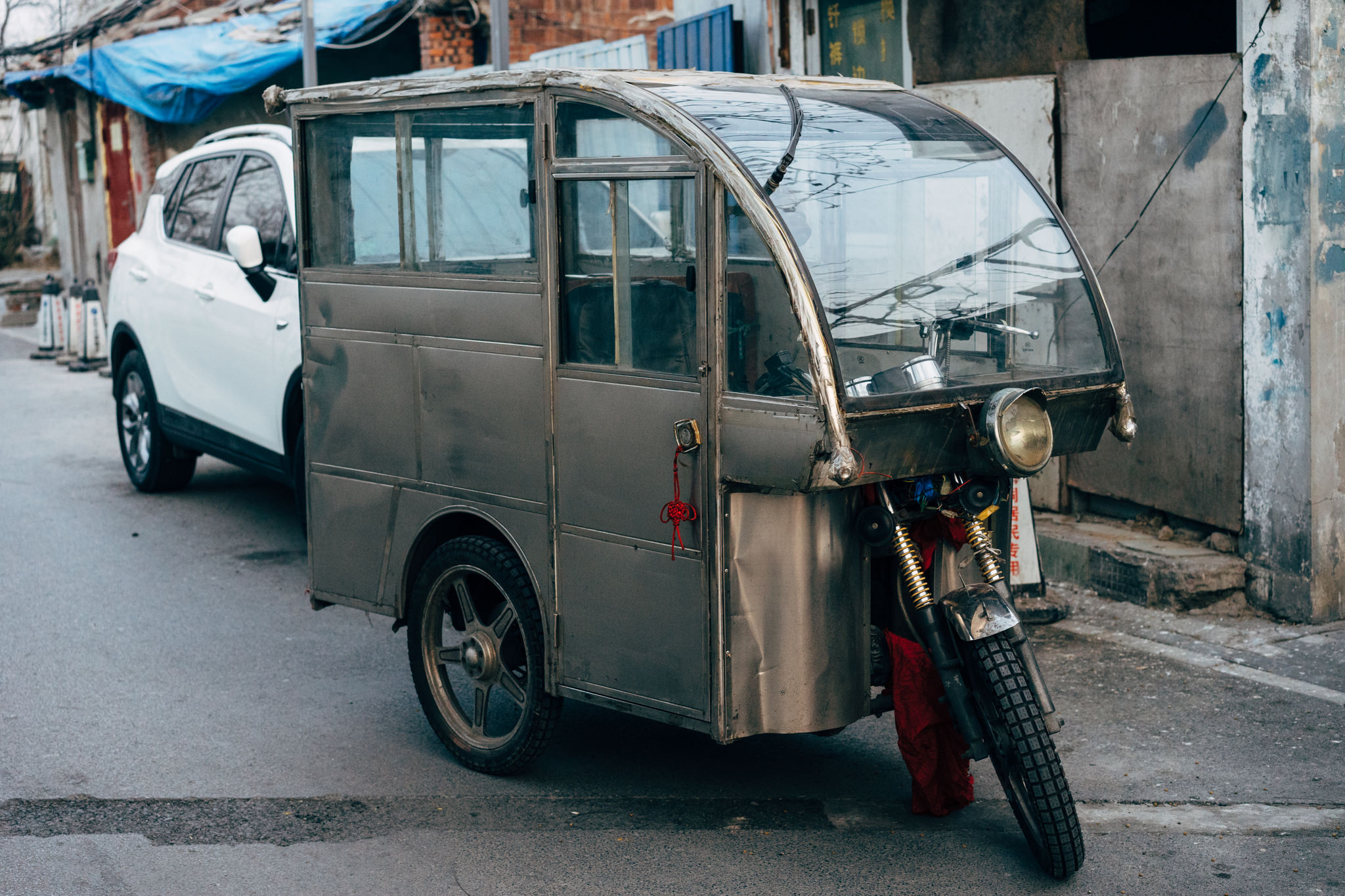 Three-wheeled electric vehicle parked next to a white SUV in Beijing.