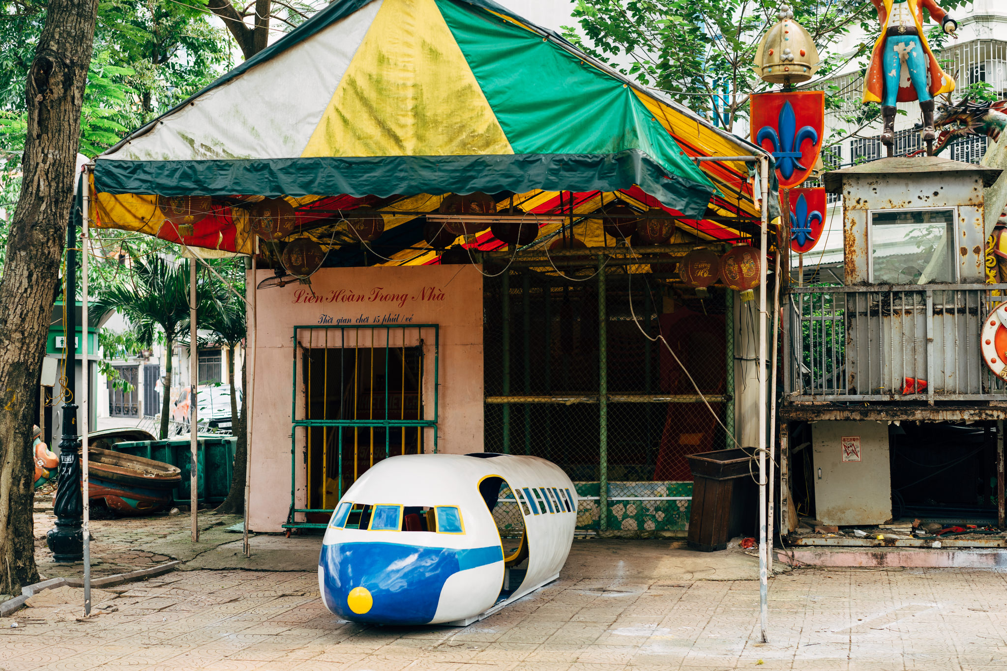 A dilapidated Hanoi amusement park ride shaped like an airplane sits under a faded awning.