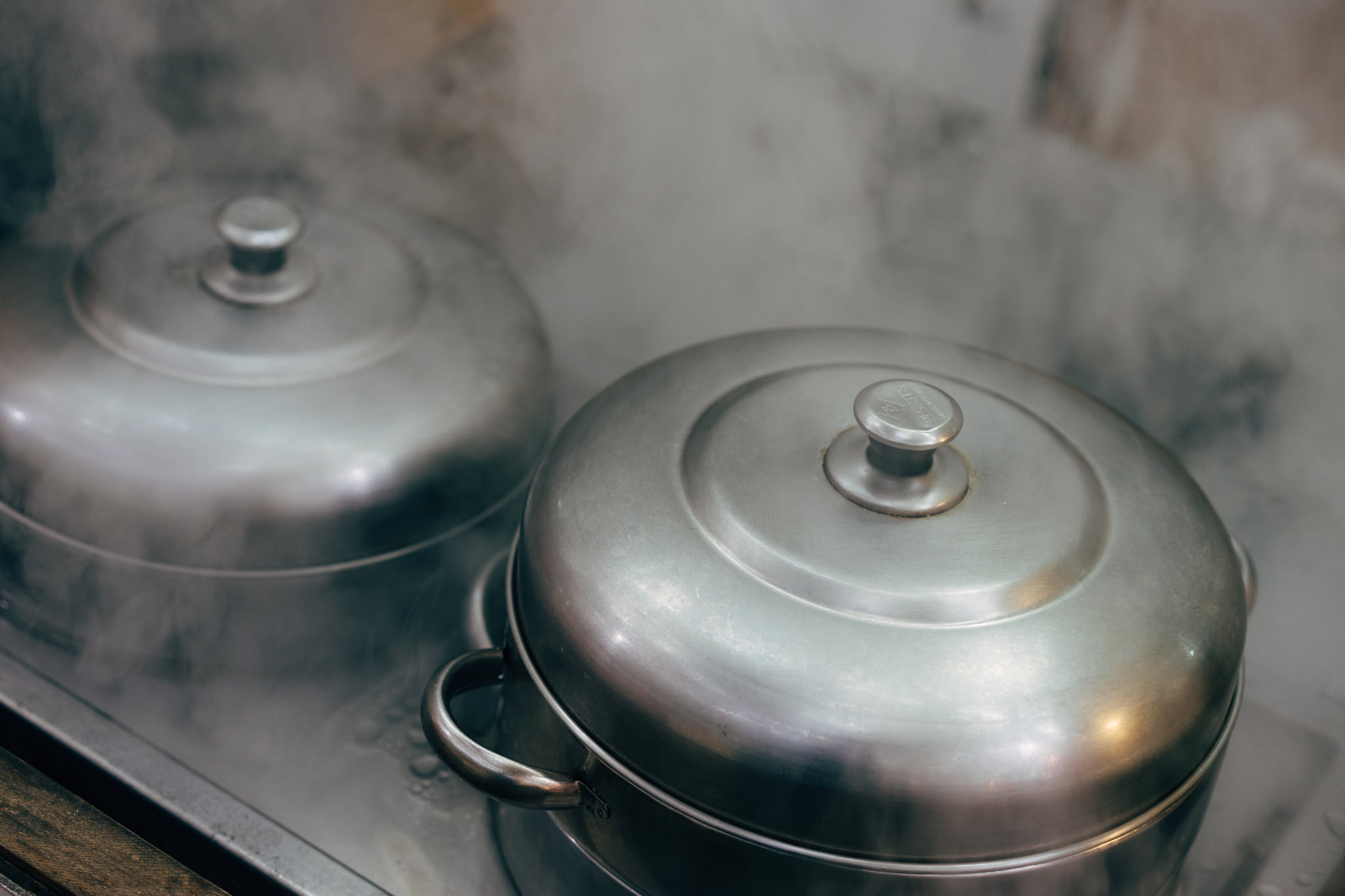 Two steaming metal pots with lids on a stove.