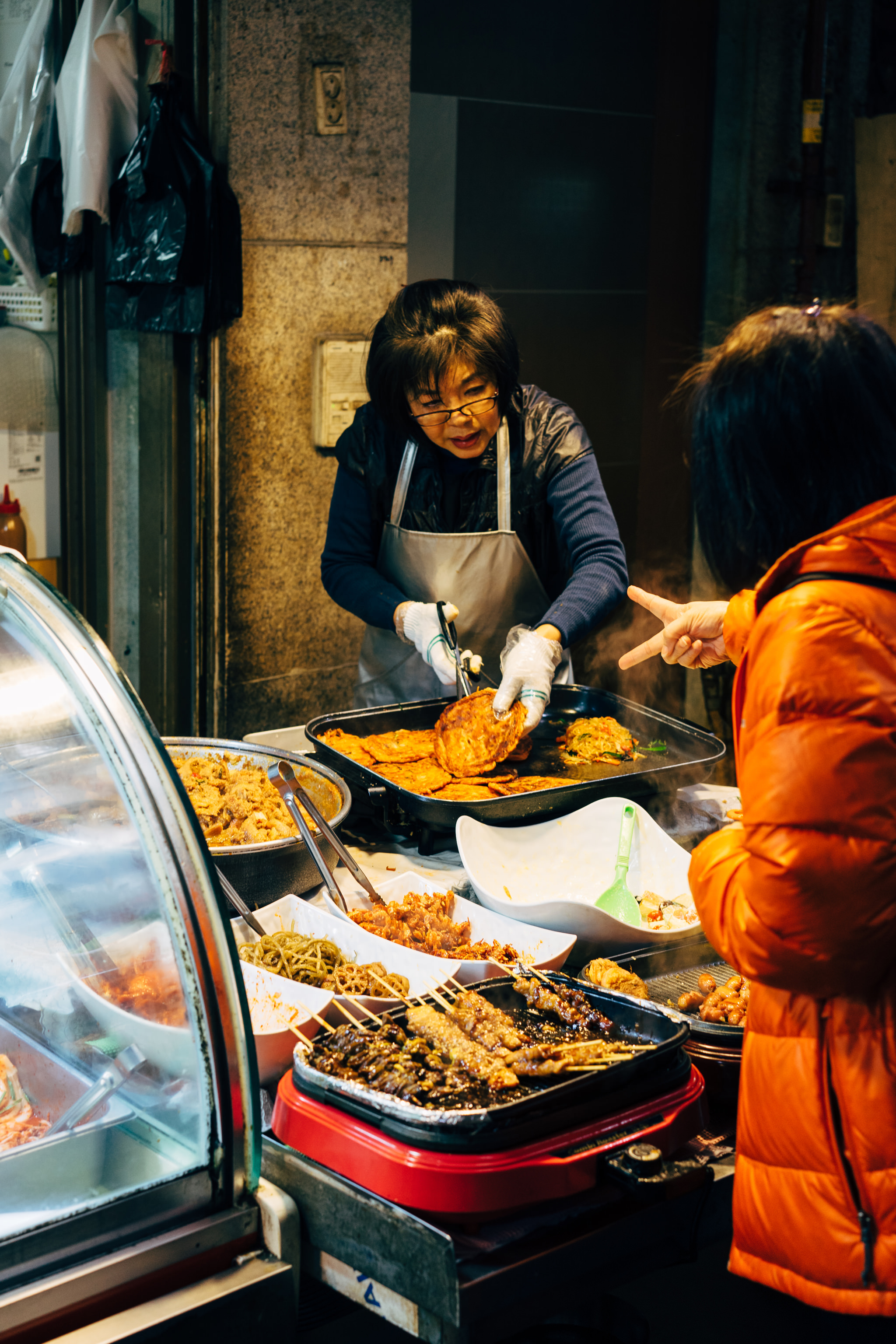 Korean street food vendor cooking and serving pancakes and other dishes.