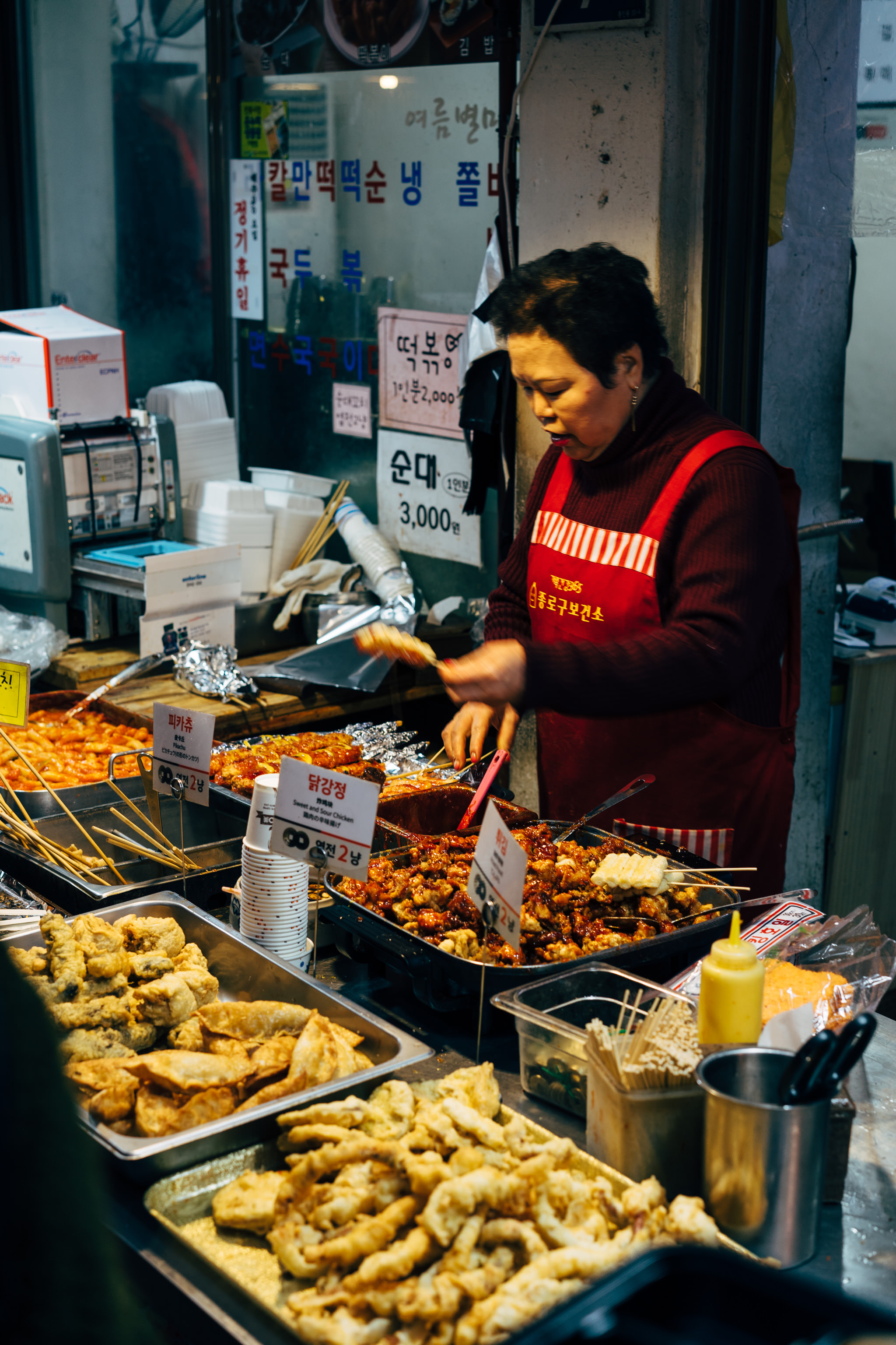 Korean street food vendor preparing and selling various fried foods and skewers.