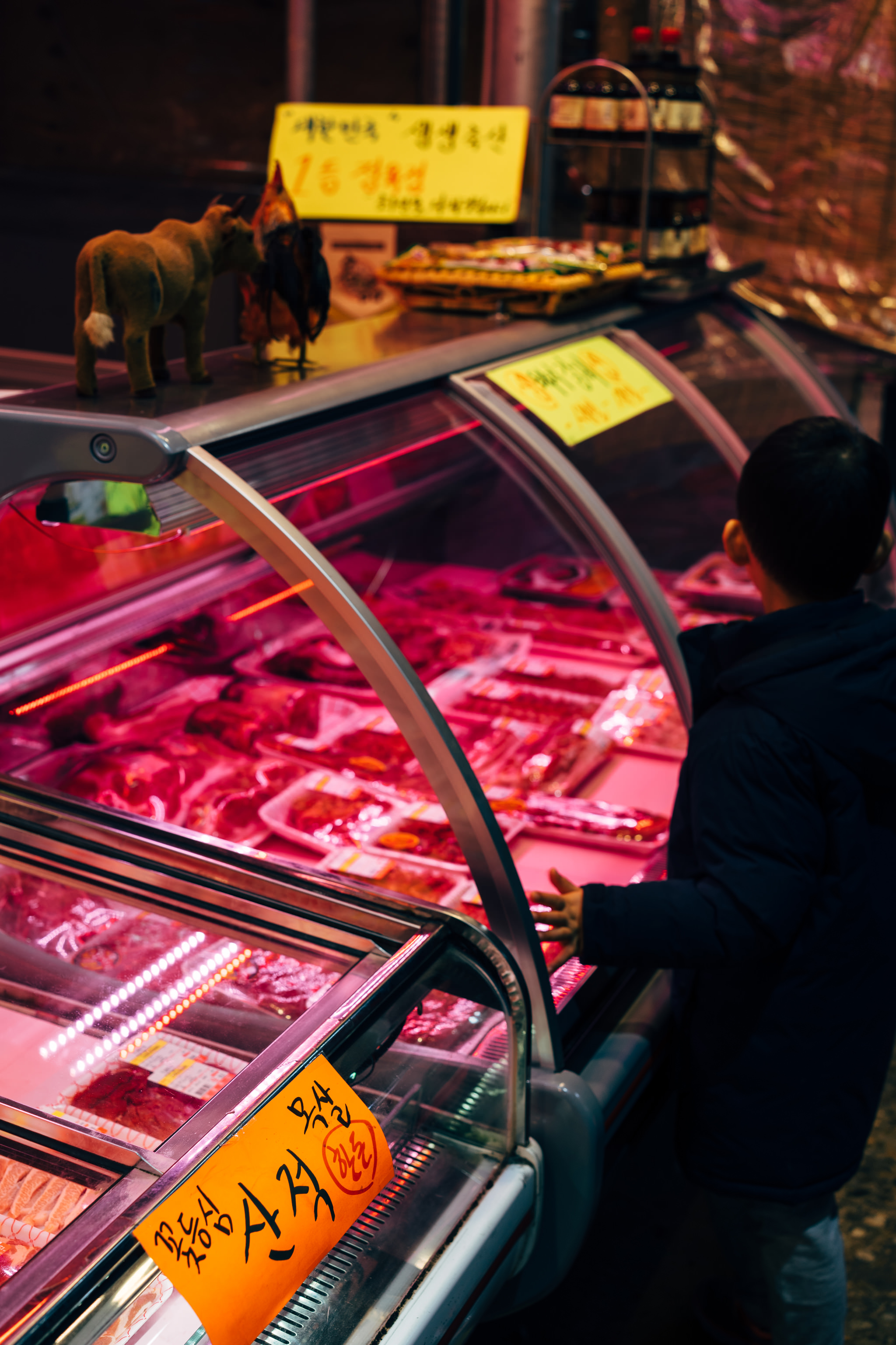 Korean butcher shop with meat displayed under pink lights in refrigerated case.
