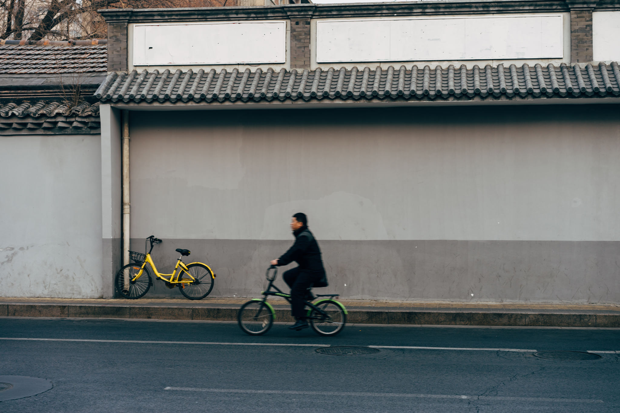 Person biking past parked yellow bicycle in Beijing.
