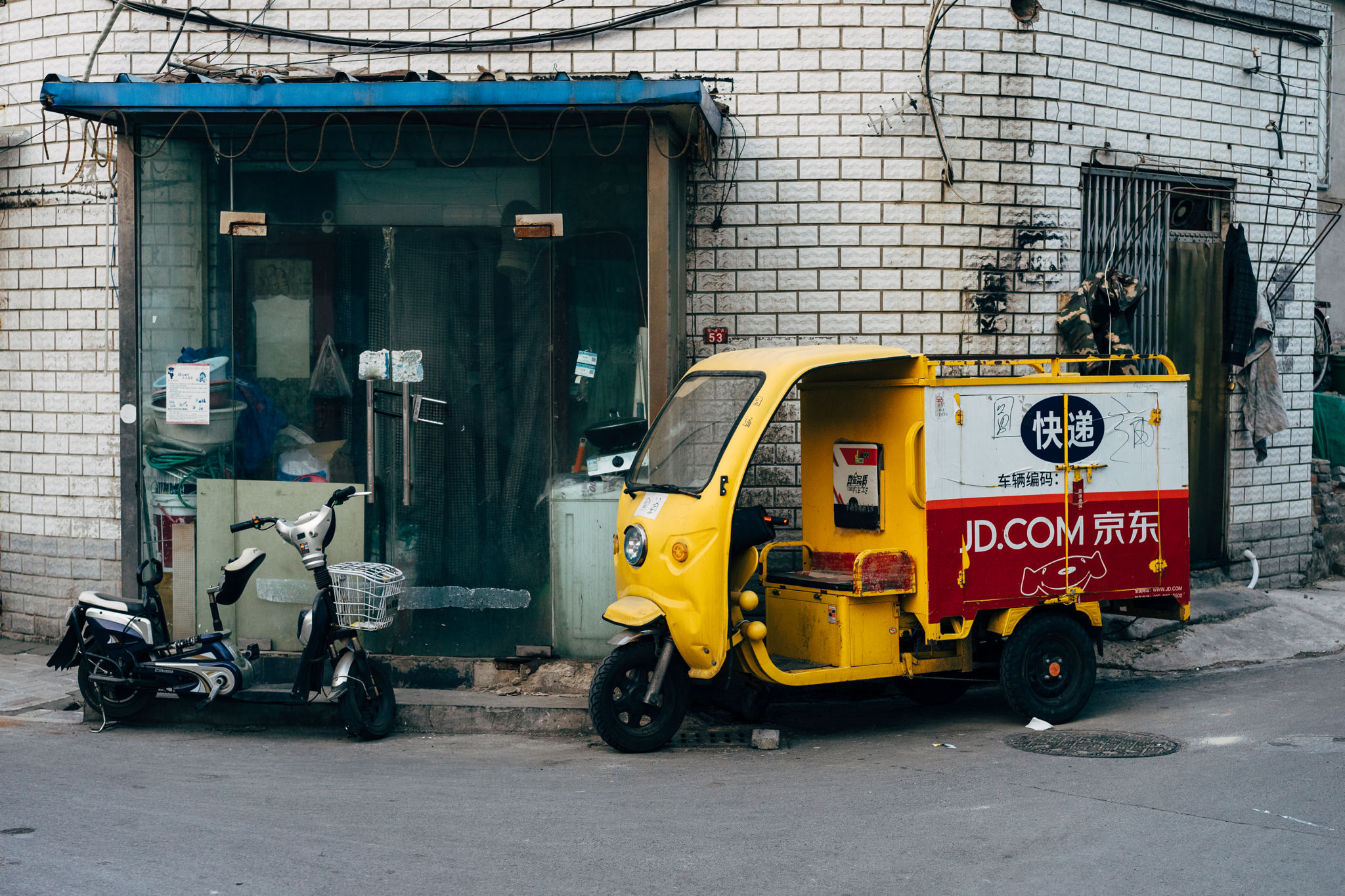 Yellow JD.com delivery vehicle parked next to an electric scooter outside a shop.