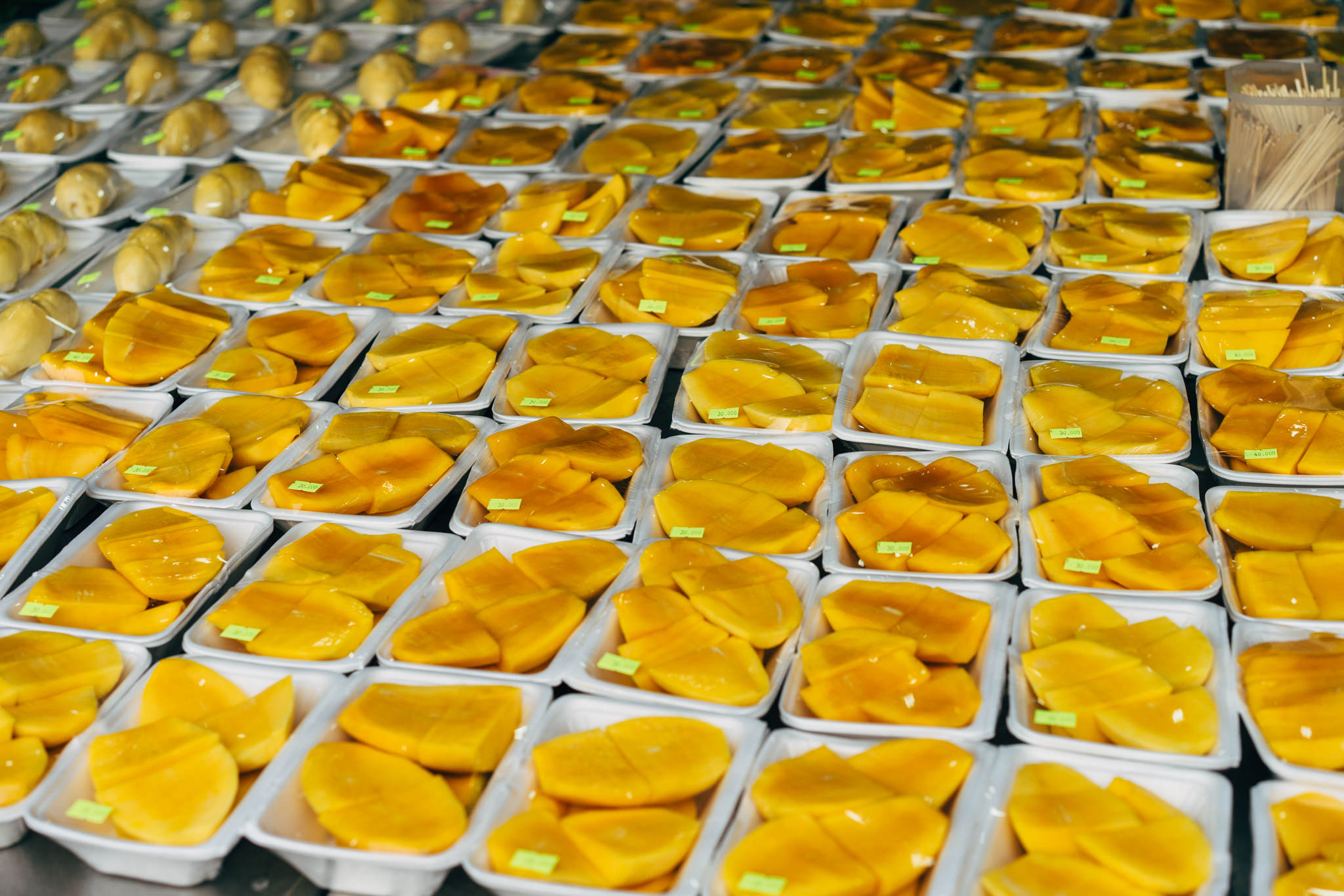 Numerous plastic containers of sliced mangoes on display.