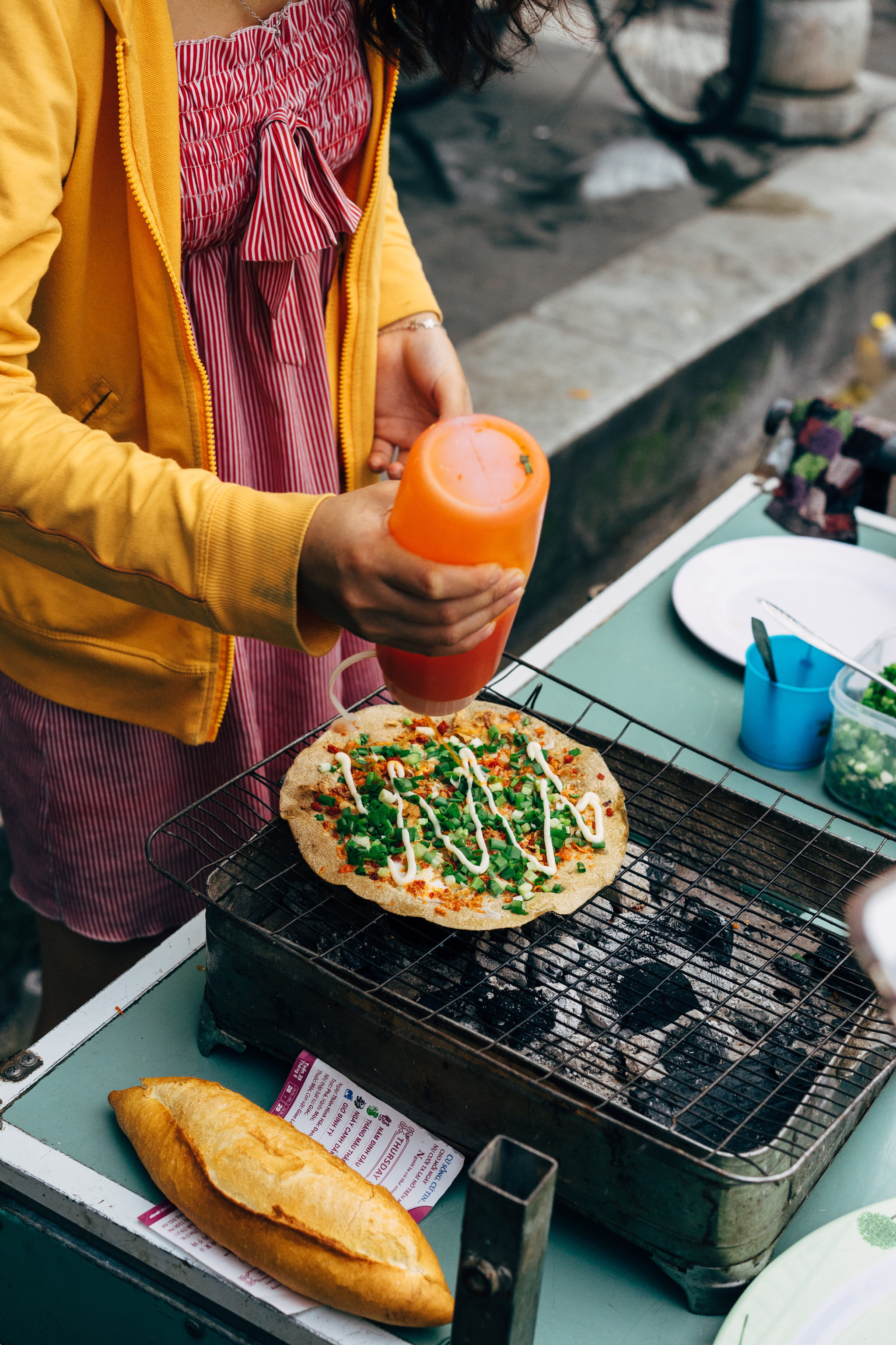 Person adding sauce to a grilled pancake topped with green onions.