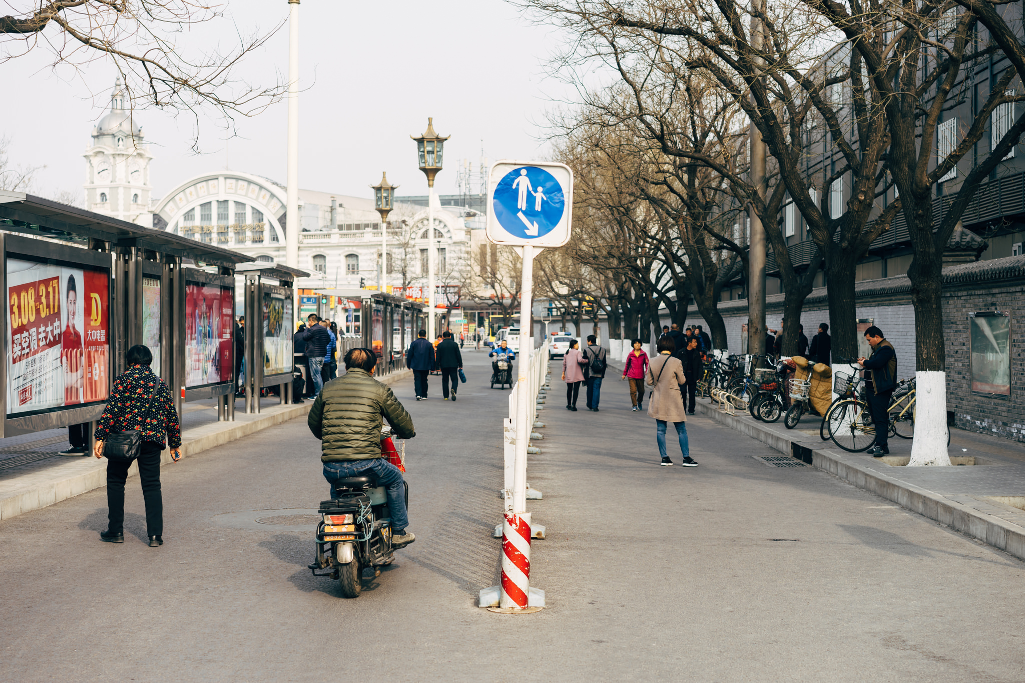 Pedestrians and a motorcyclist on a Beijing street, with a pedestrian and child crossing sign.