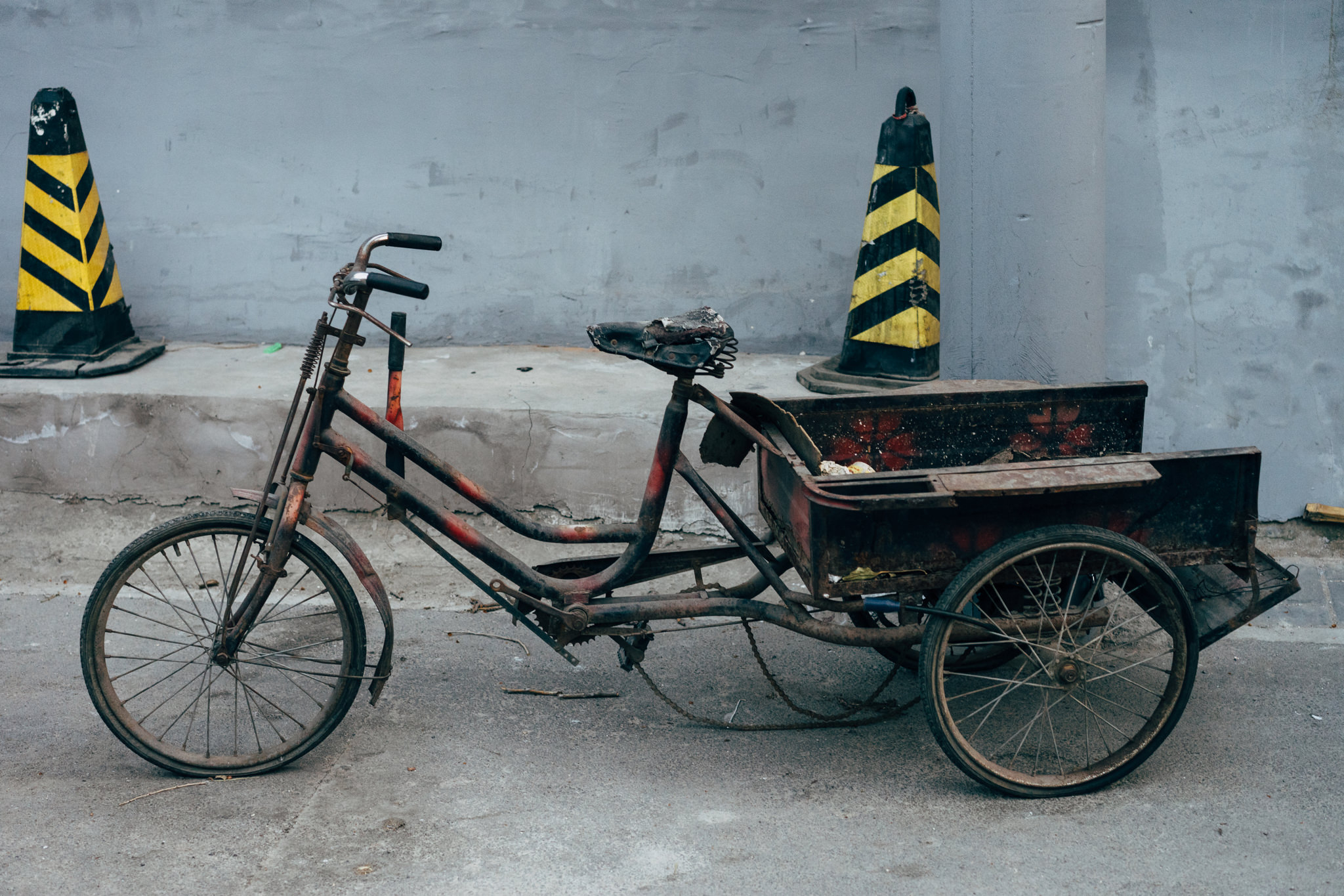 Rusty old tricycle with cargo bed parked against a wall.