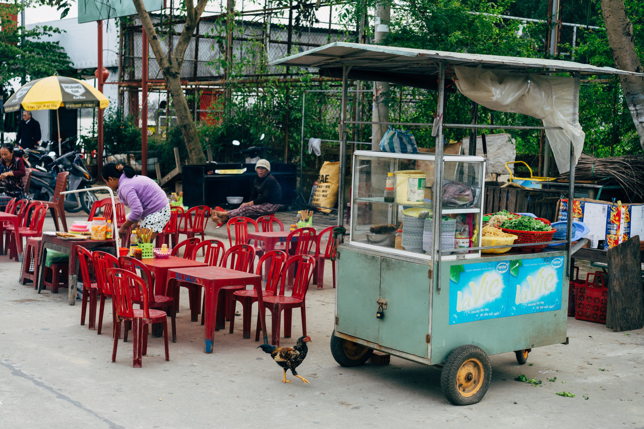 Outdoor food stall with red plastic chairs and tables.
