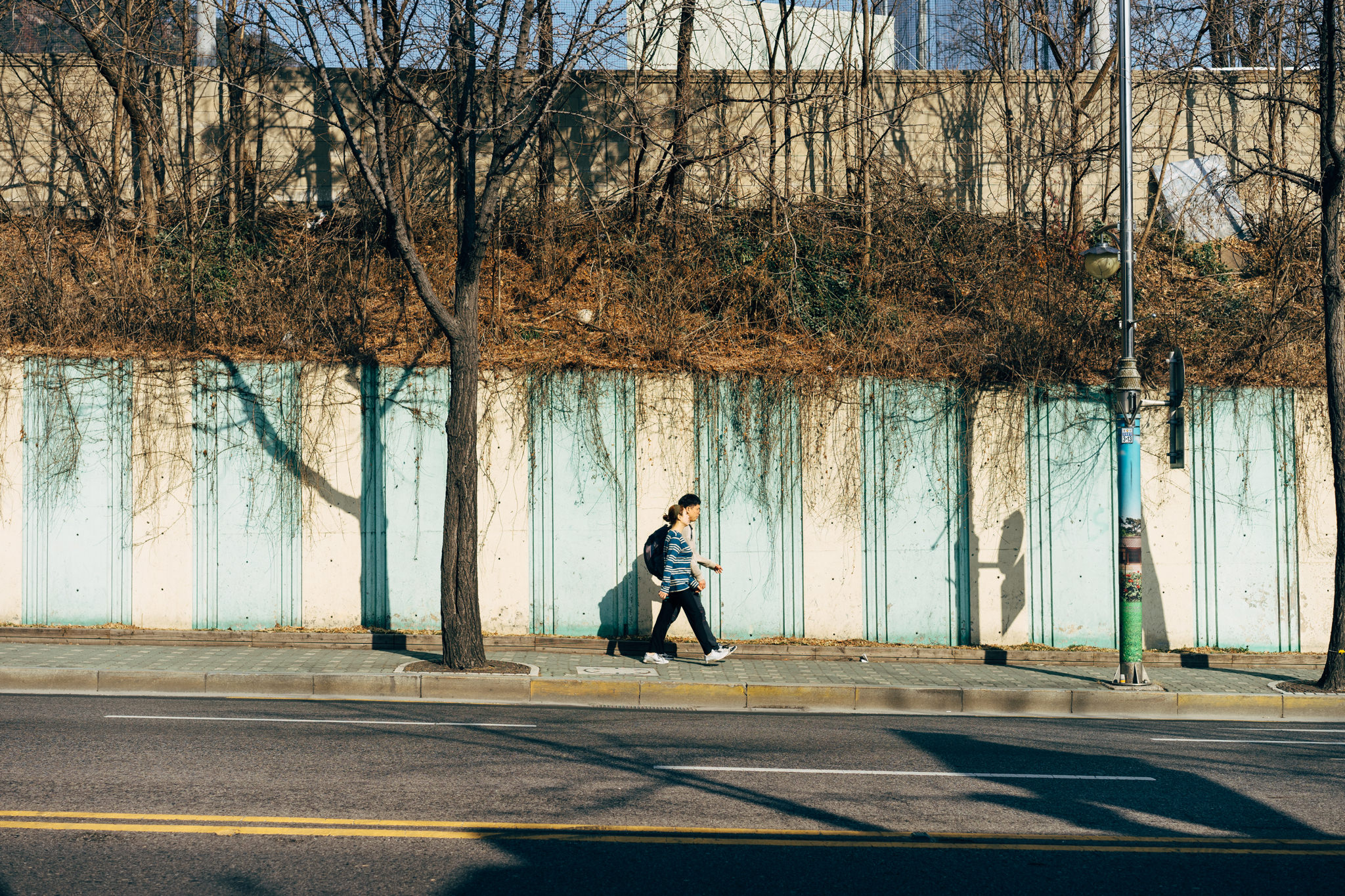 Person walking on a city sidewalk next to a wall.