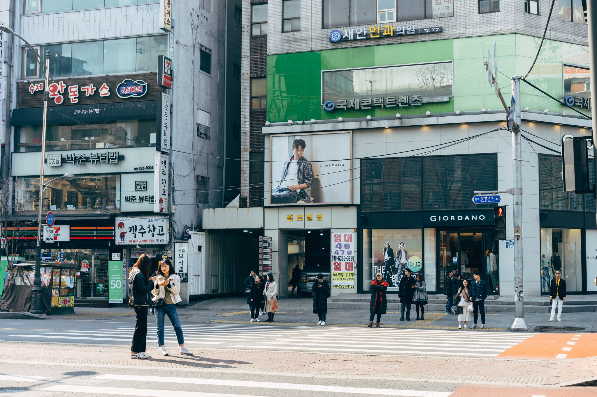 Pedestrians crossing a street in Seoul, South Korea, in front of a Giordano clothing store.