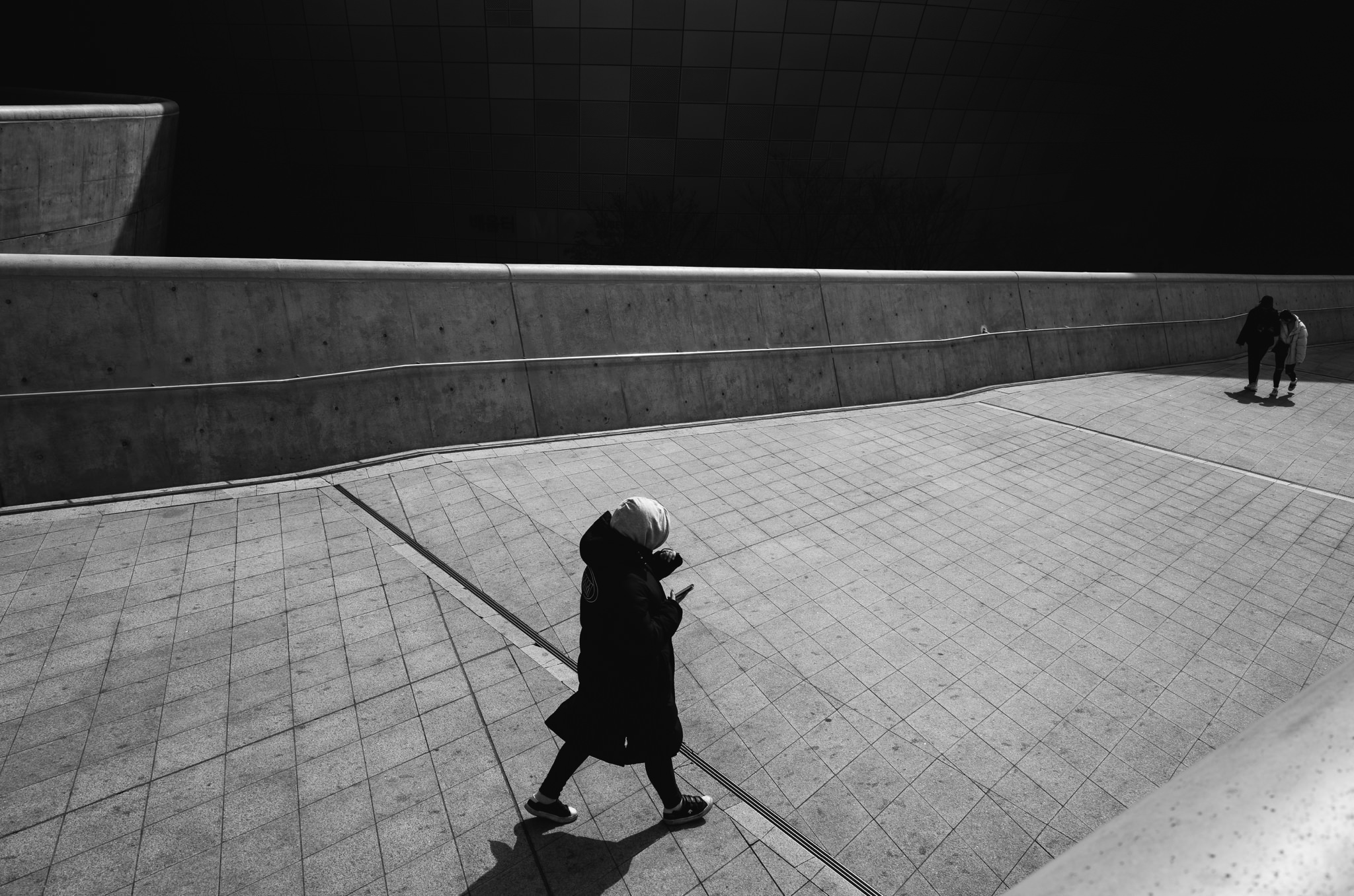 Black and white photo of a person walking on a paved area in Seoul, South Korea, looking at their phone.
