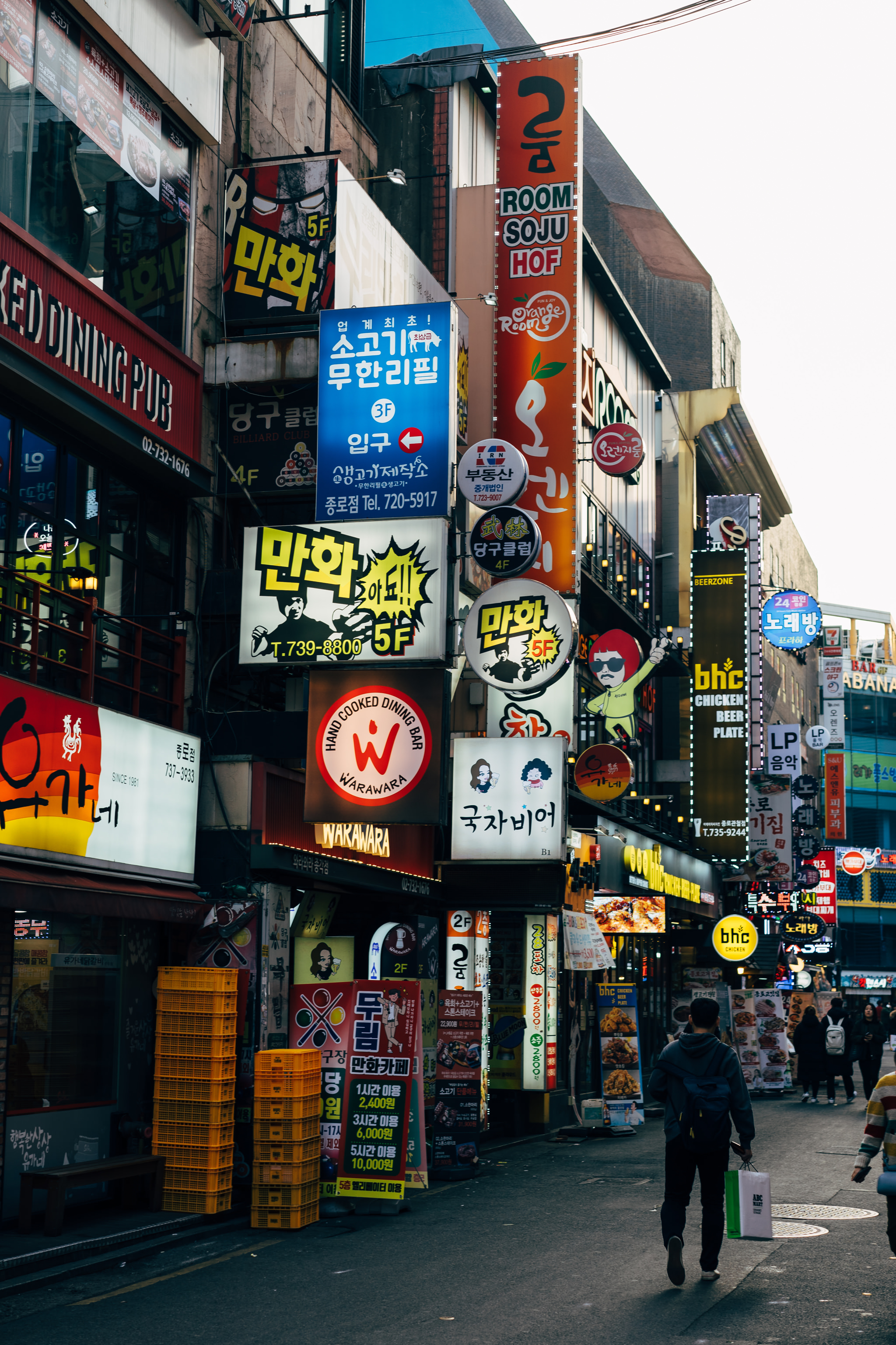A bustling Seoul street scene with numerous brightly lit Korean restaurant and bar signs.