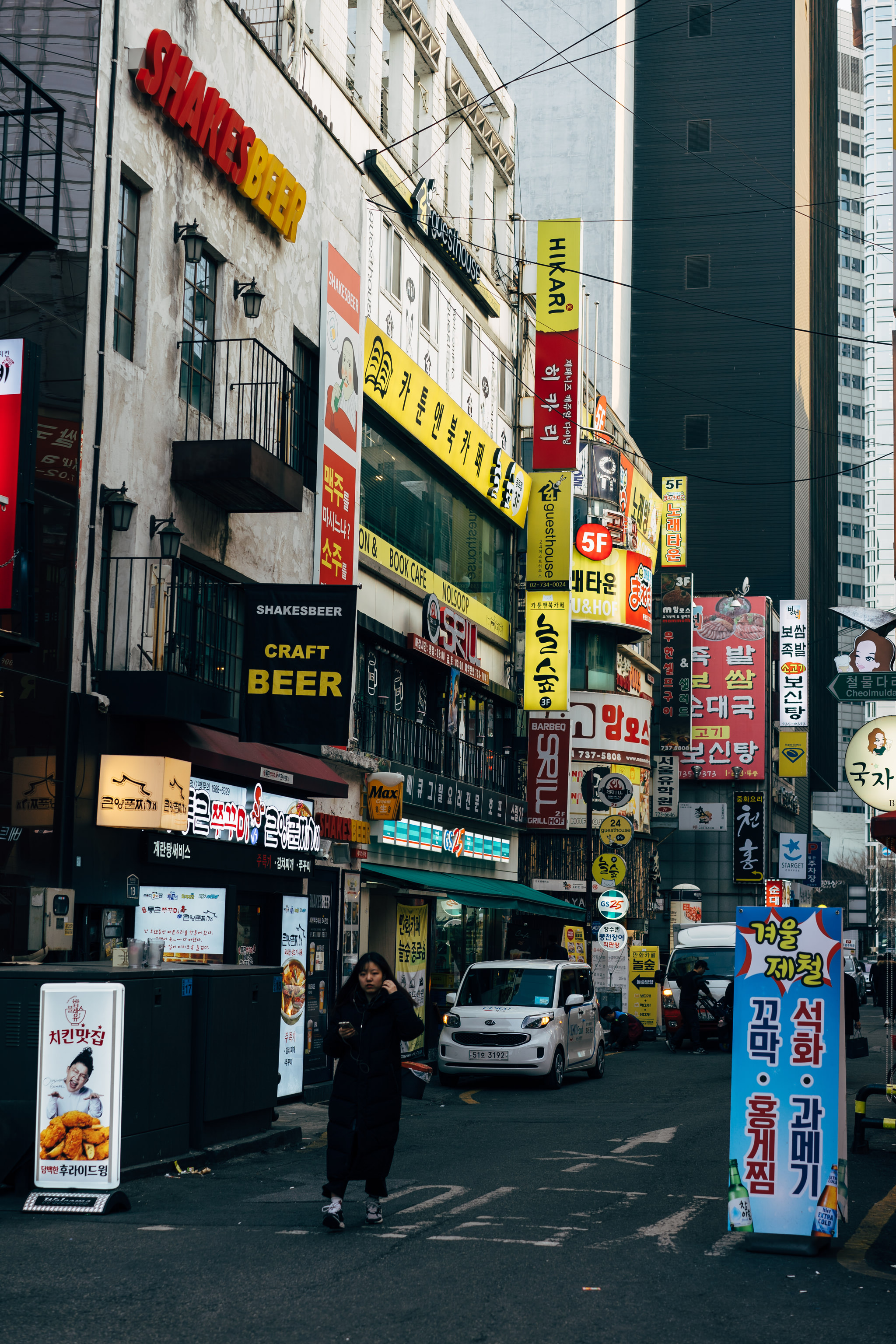 A bustling Seoul street scene with numerous shops and signs in Korean and English.
