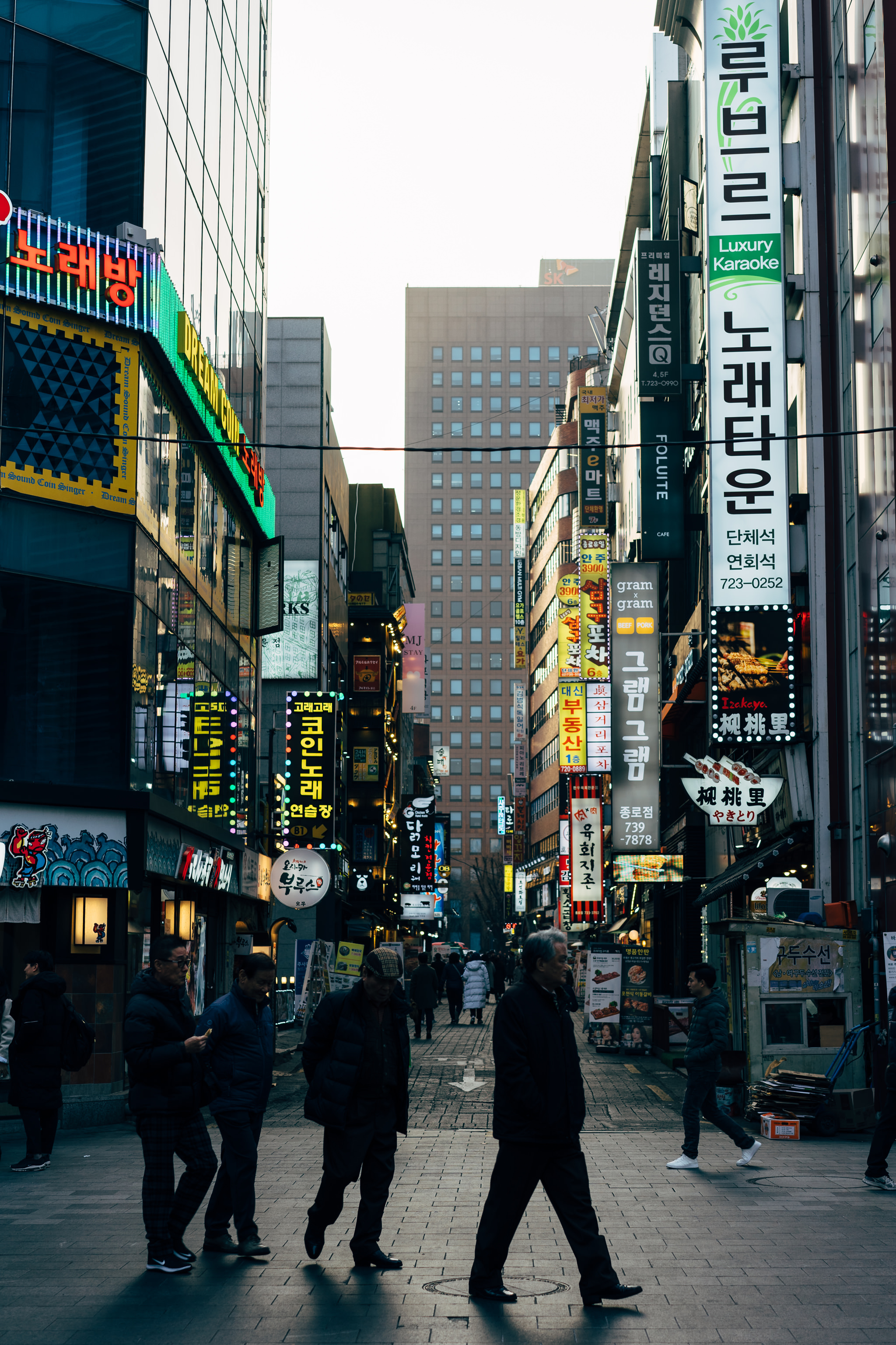 Busy Seoul street scene with pedestrians and brightly lit storefronts.