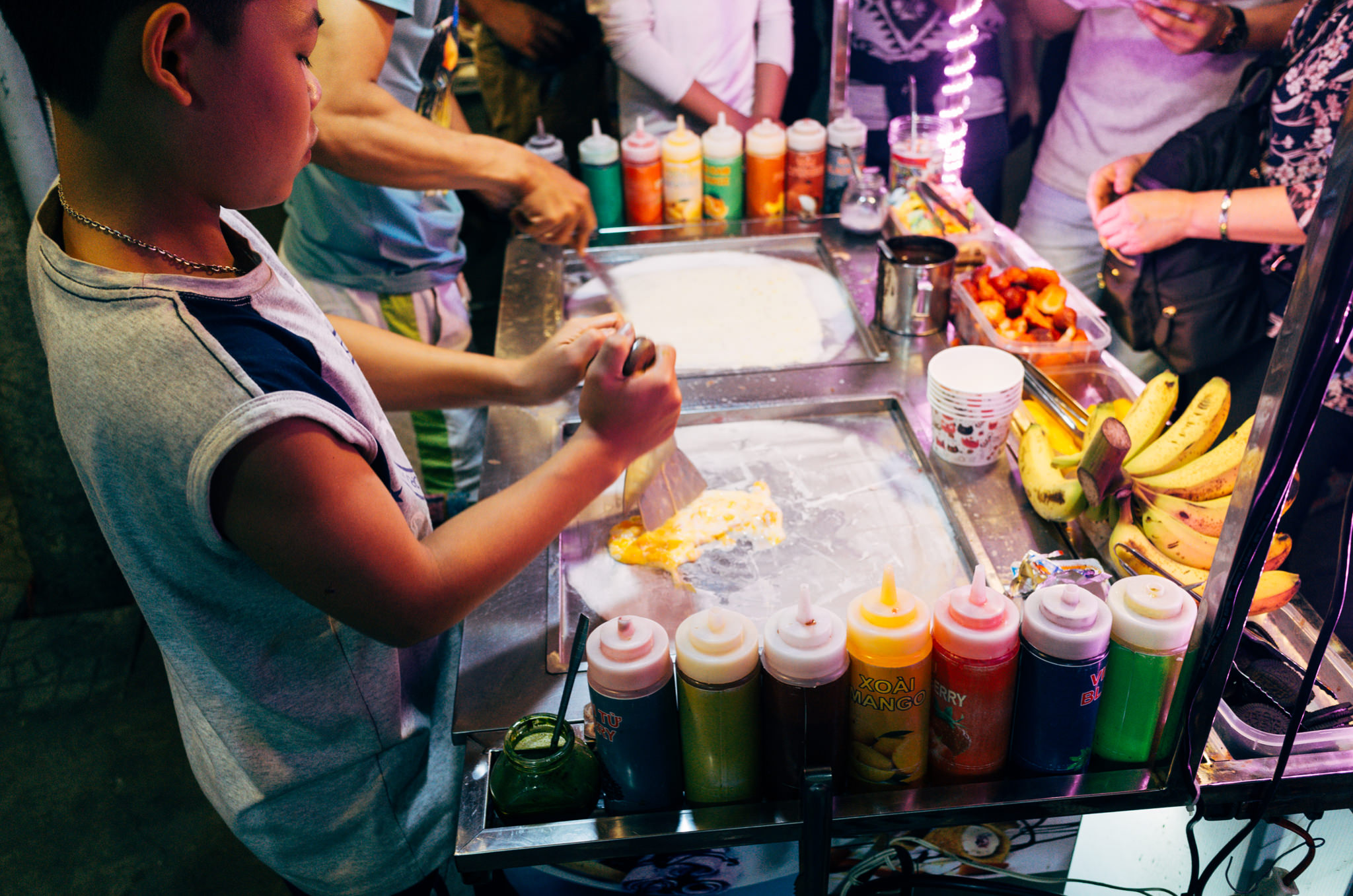 A child prepares rolled ice cream at a street food stall.