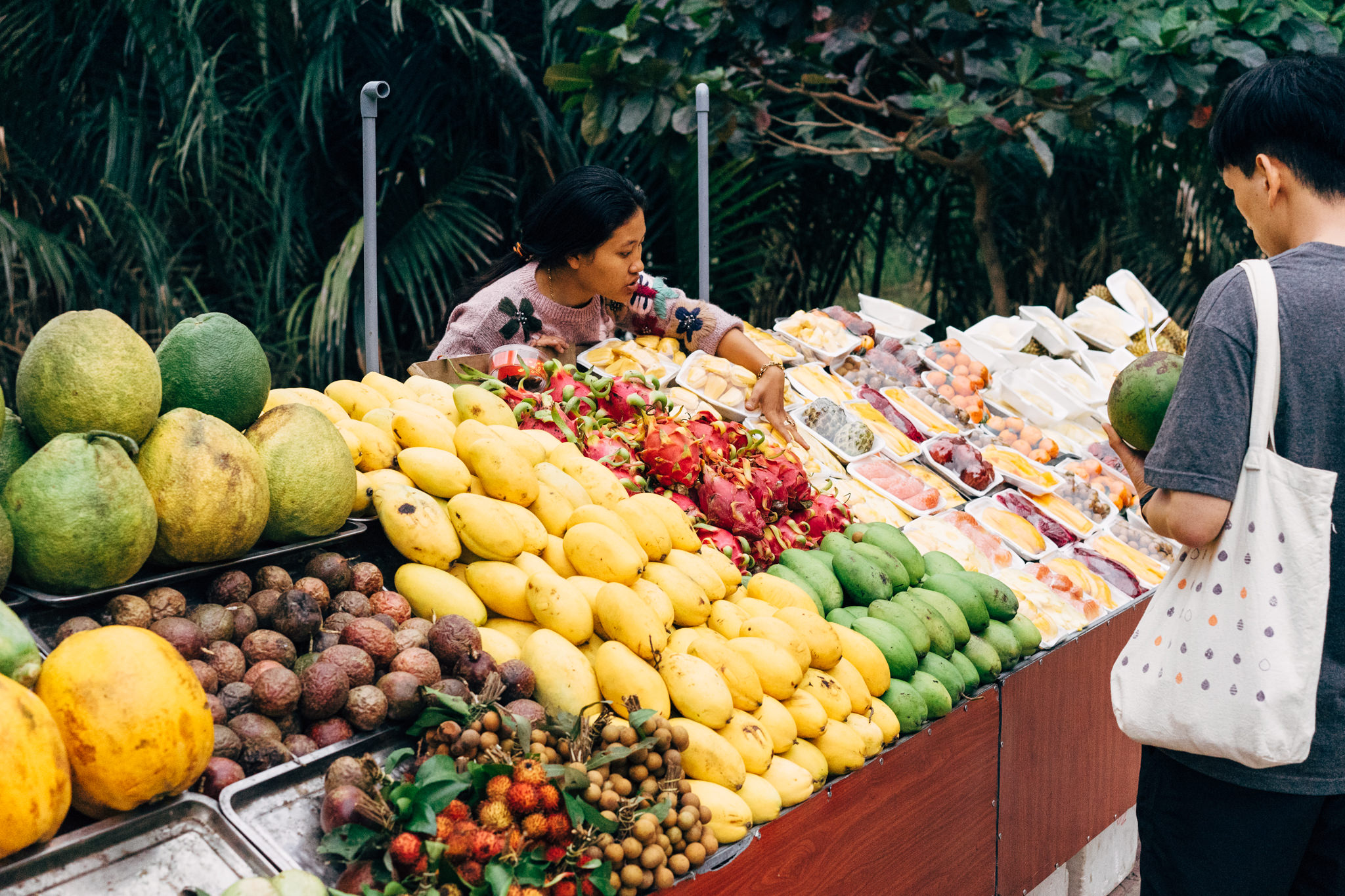A woman shops for mangoes, dragon fruit, and other tropical fruits at an outdoor market in Hoi An.
