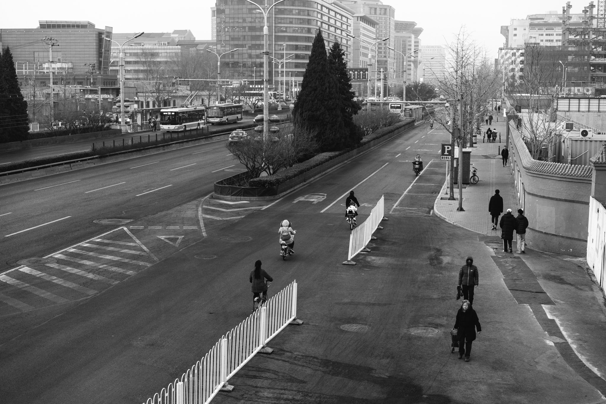 Black and white photo of a mostly empty street scene in China with pedestrians and cyclists.