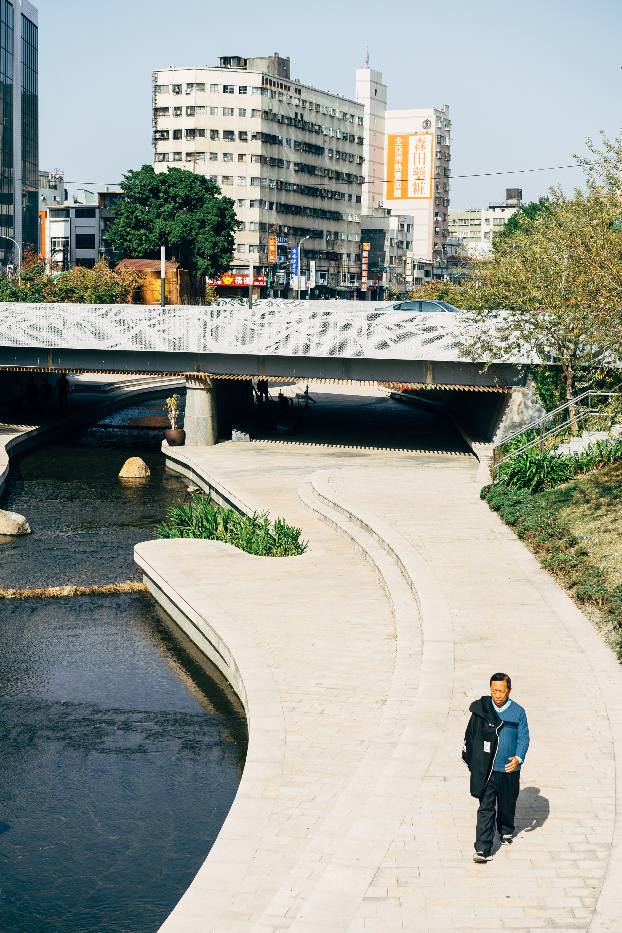 Man walking along a paved path next to a canal in Taichung City.