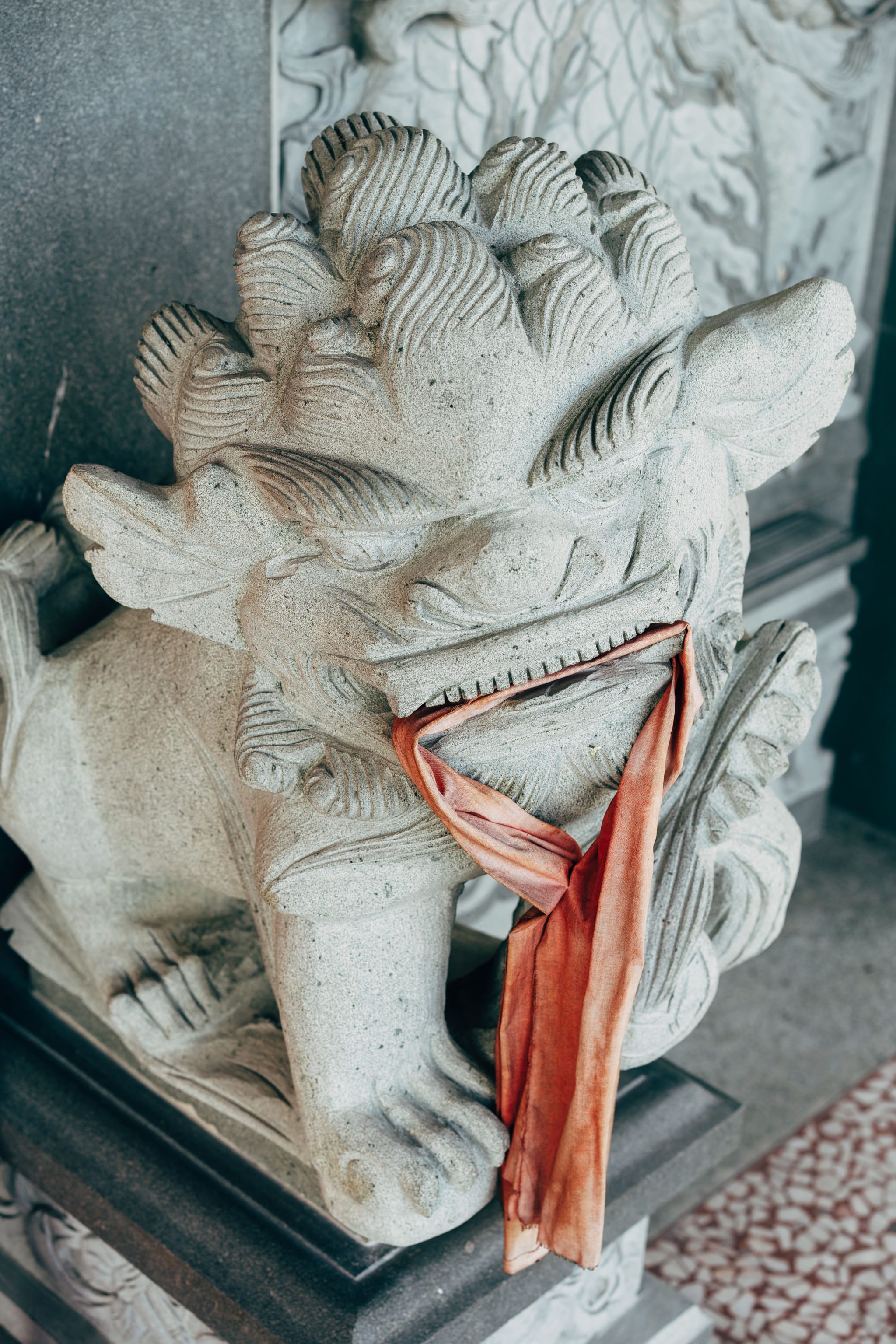 Stone lion statue with orange cloth in its mouth.